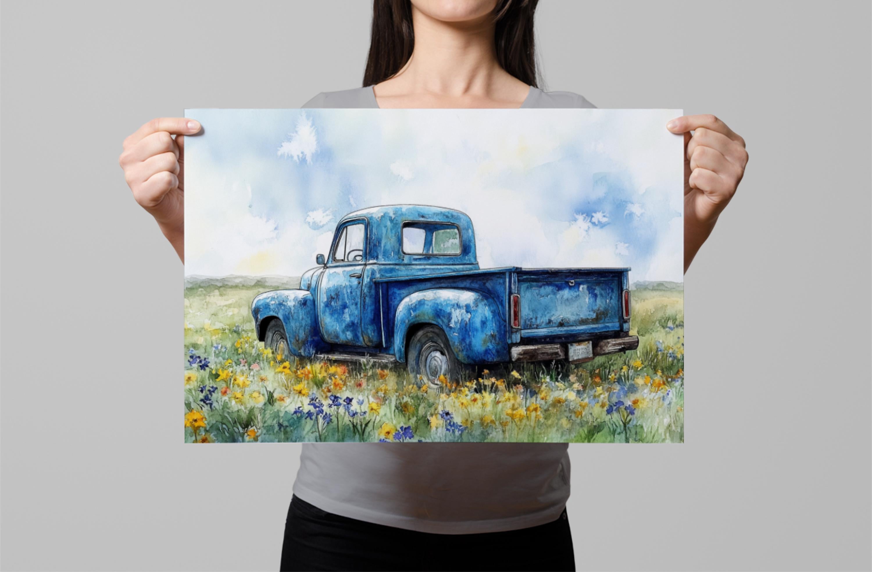 A woman holds up a framed painting of an old blue pickup truck parked in a field of flowers.