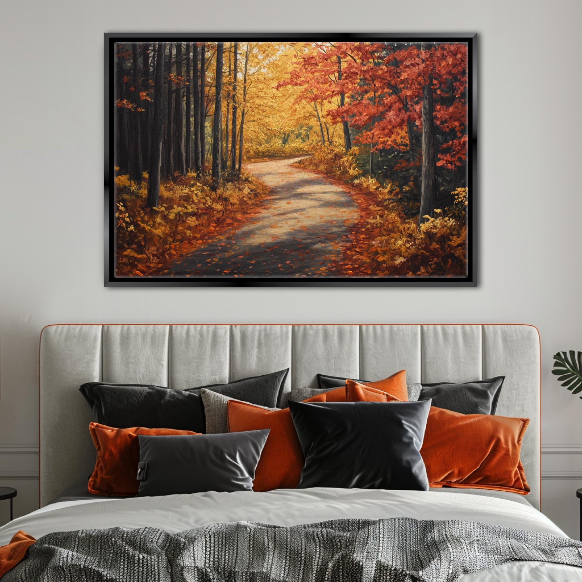 a large framed painting of a forest path with autumn foliage, hanging above a bed with a gray headboard and colorful pillows.