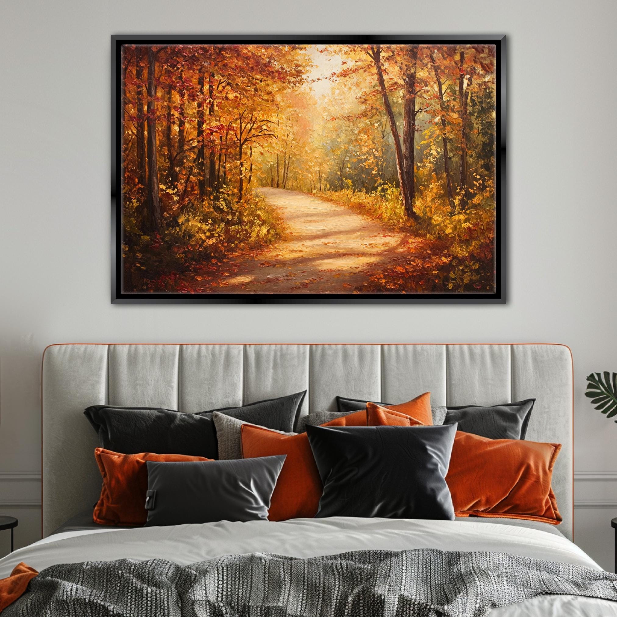 a large painting of a forest path with autumn foliage hanging above a bed with a gray headboard and colorful pillows.