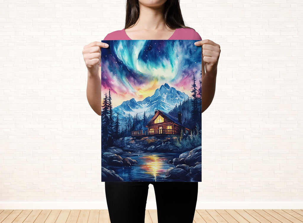 A woman holds up a poster featuring a cabin surrounded by a forest and mountains, with a colorful night sky above.