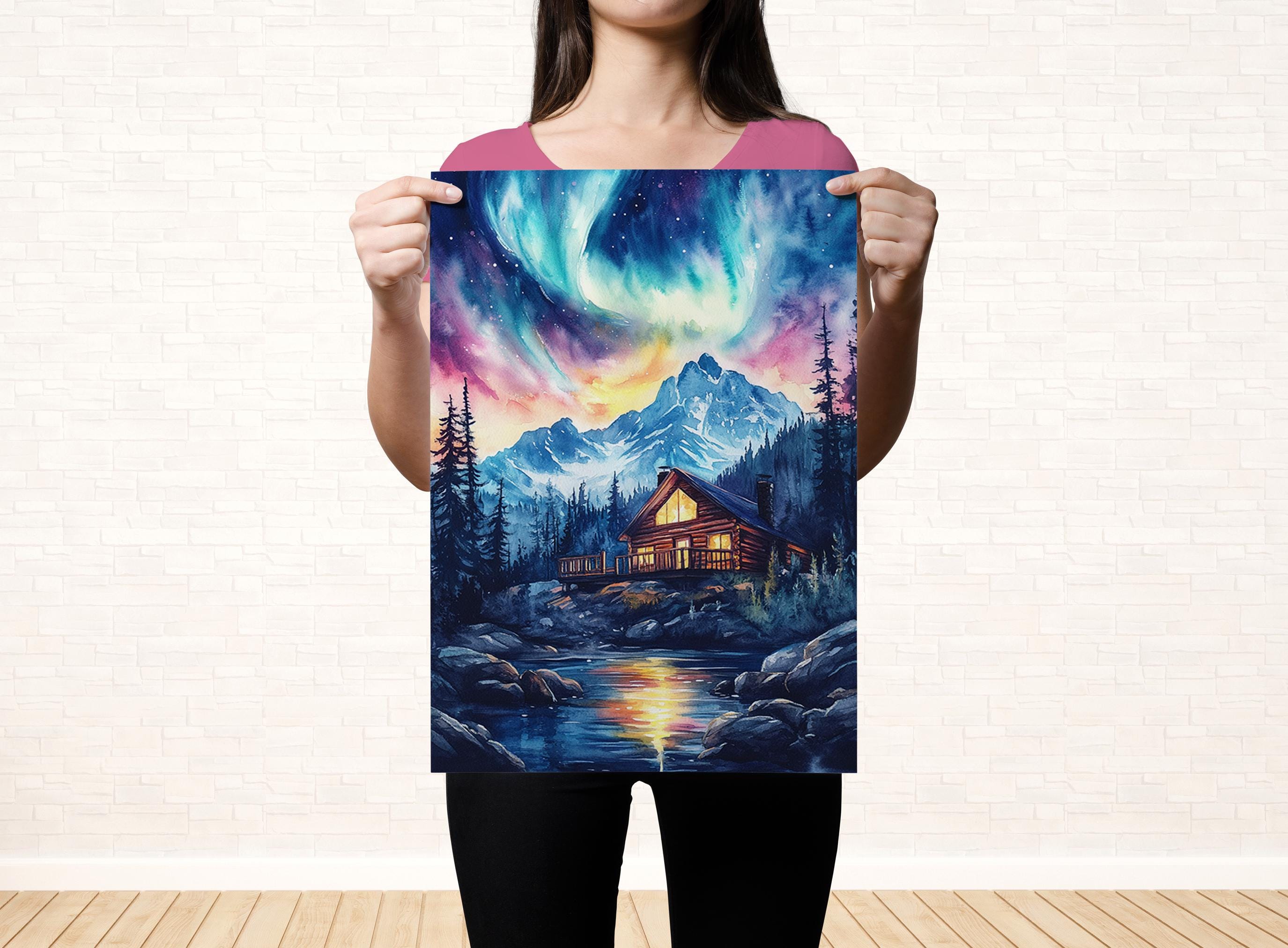 A woman holds up a poster featuring a cabin surrounded by a forest and mountains, with a colorful night sky above.