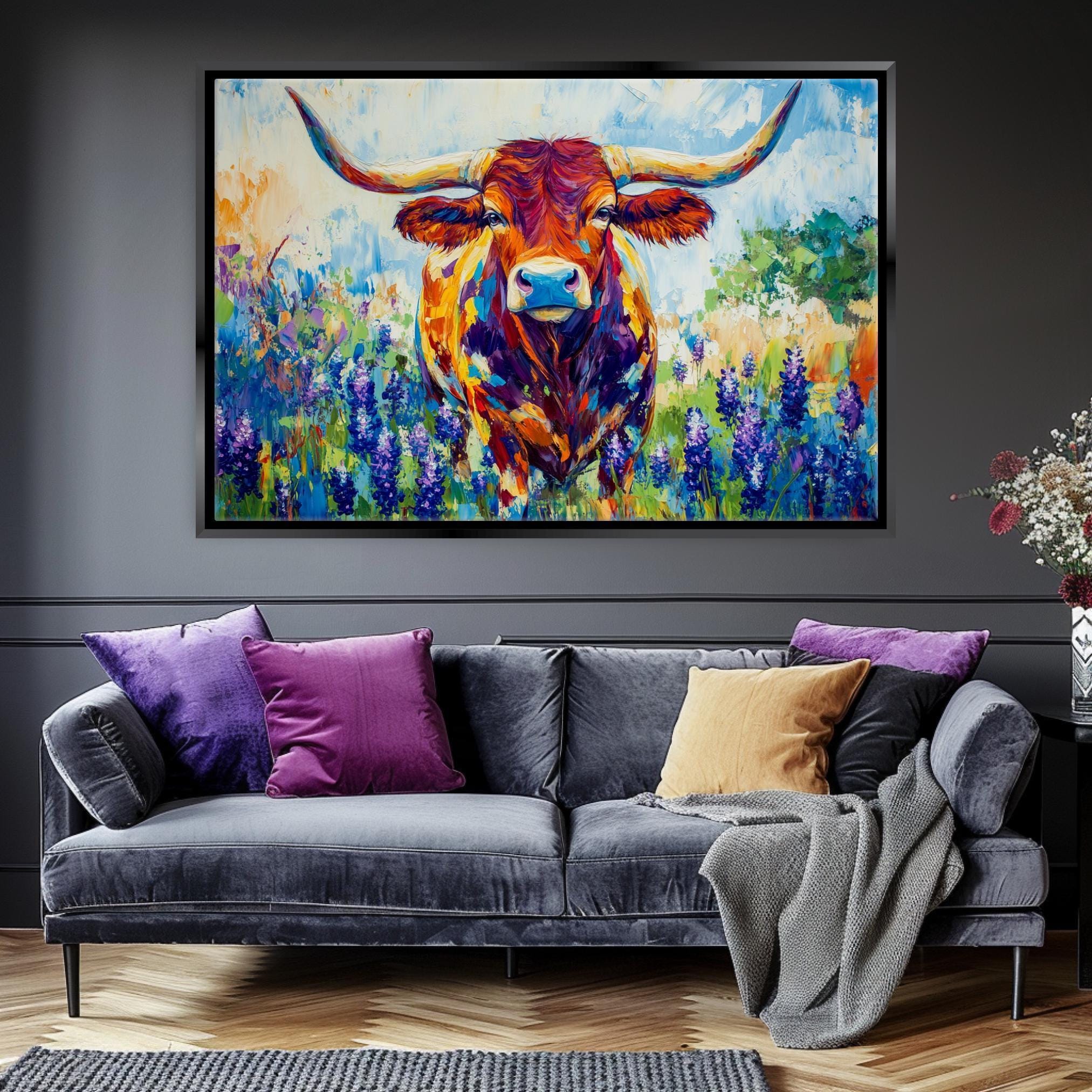 a large, colorful painting of a bull with horns hanging on a wall above a gray couch with purple and yellow throw pillows.