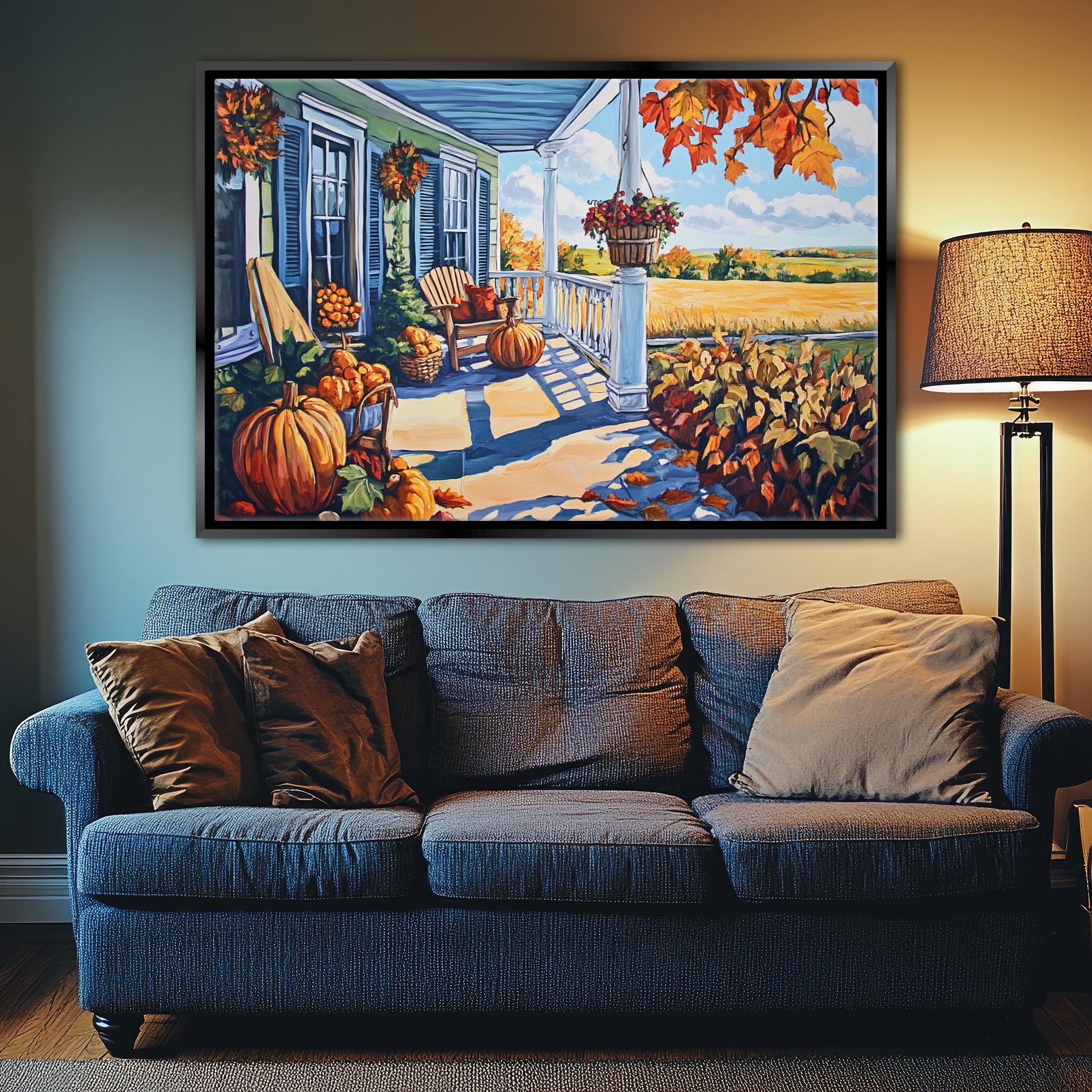a large painting of a porch with a blue house, pumpkins, and fall foliage displayed on the wall above a blue couch with pillows.