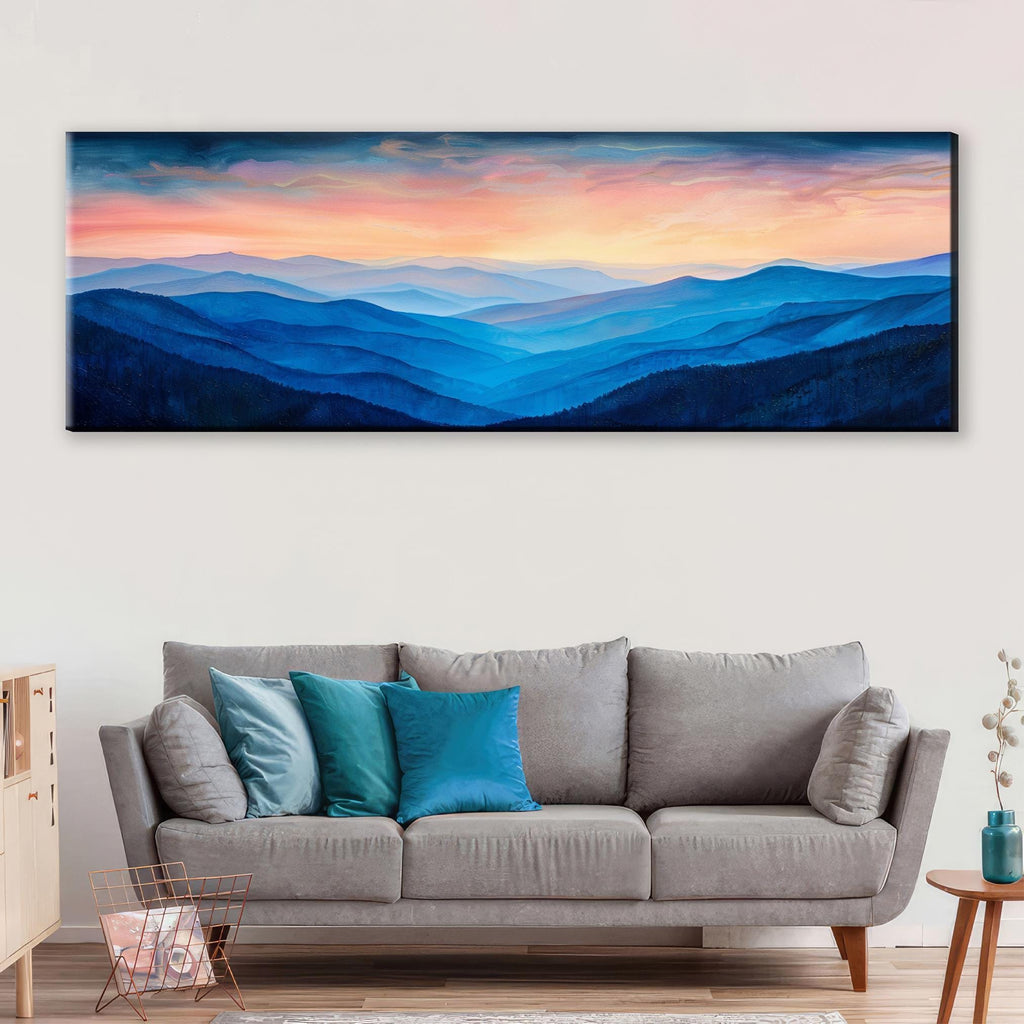 a large, long painting of a mountain range with a colorful sunset sky above it. The painting is hanging on a wall above a gray sofa with blue and teal throw pillows.