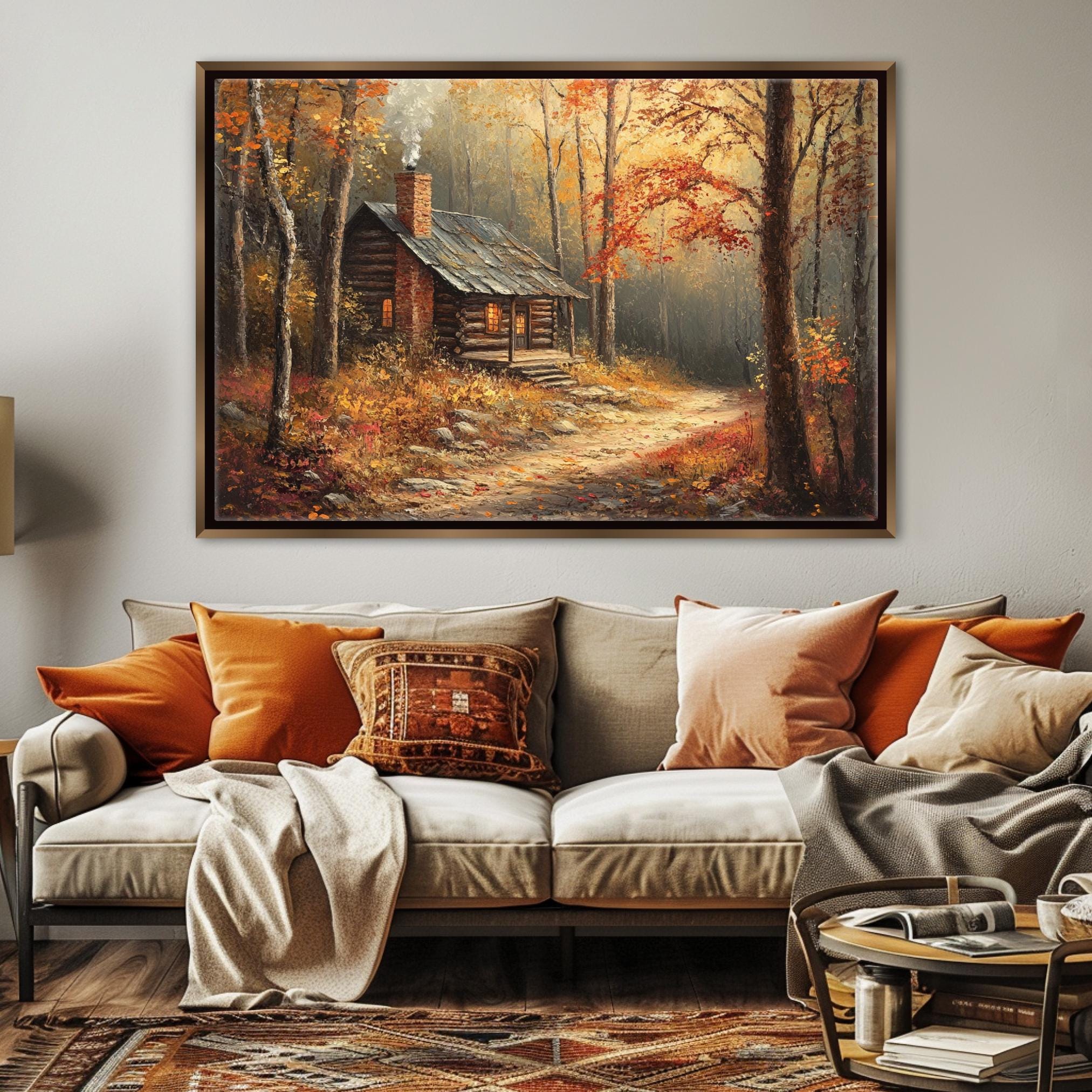 a cozy cabin nestled in a forest, with a path leading up to it. The cabin is surrounded by trees with vibrant autumn foliage, creating a warm and inviting atmosphere. The cabin is situated on a dirt path, adding to the rustic charm of the scene. The image is framed and hung on a wall, serving as a focal point in the living room.
