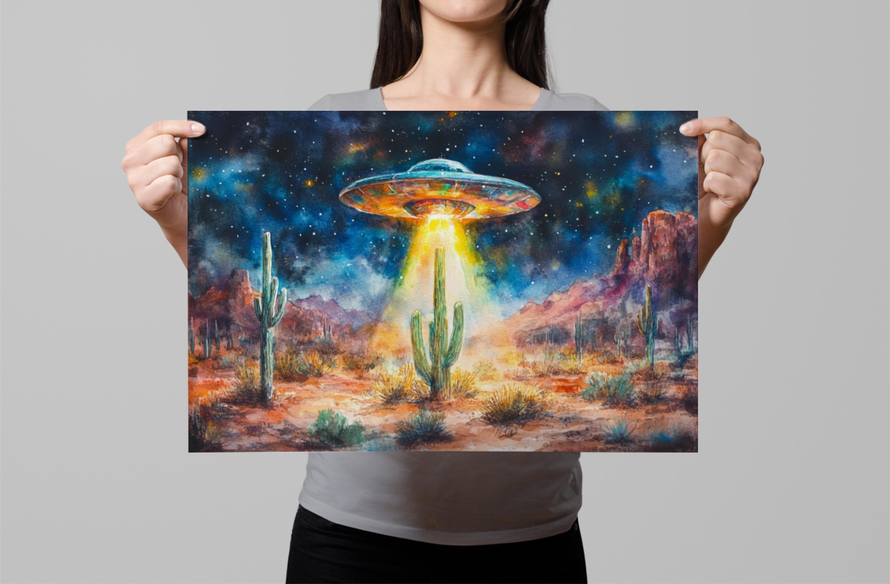 A woman holds up a painting depicting a desert landscape with a large alien spacecraft hovering above the cacti and mountains.