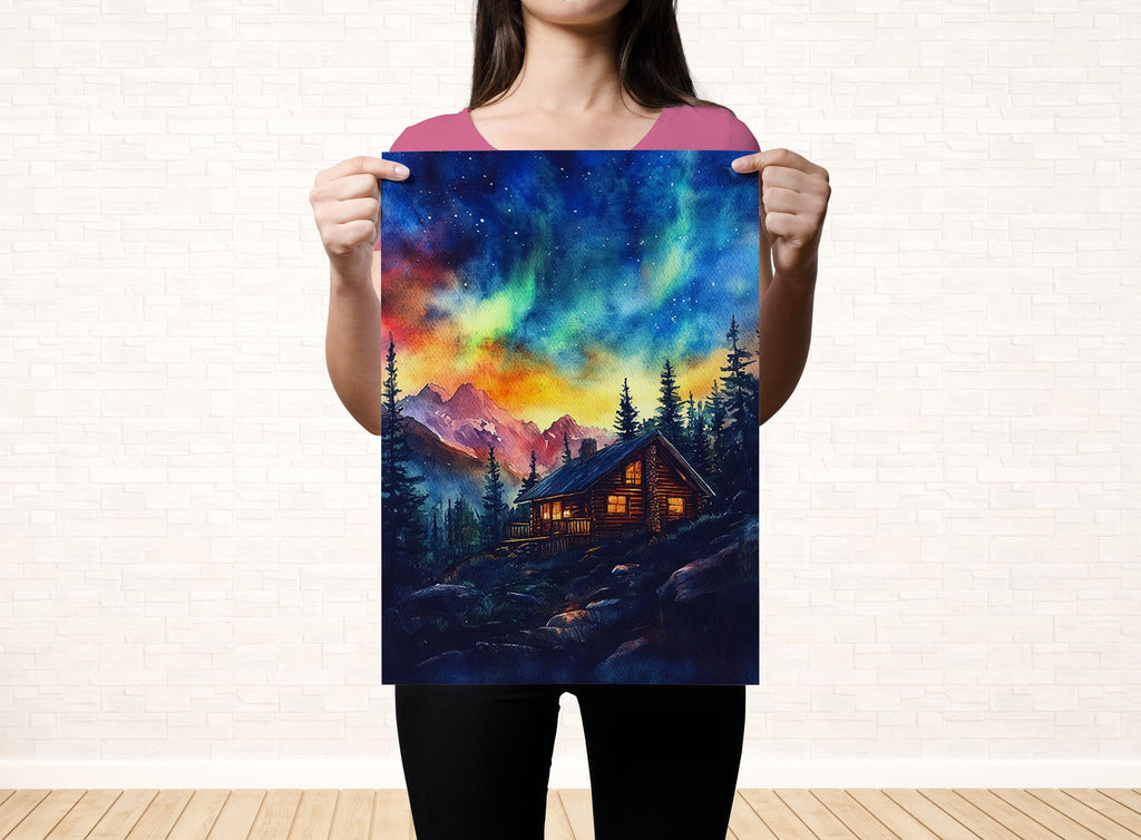 A woman holds up a vibrant painting depicting a cabin nestled in a mountainous landscape, with a stunning night sky filled with colorful stars and the Aurora Borealis.