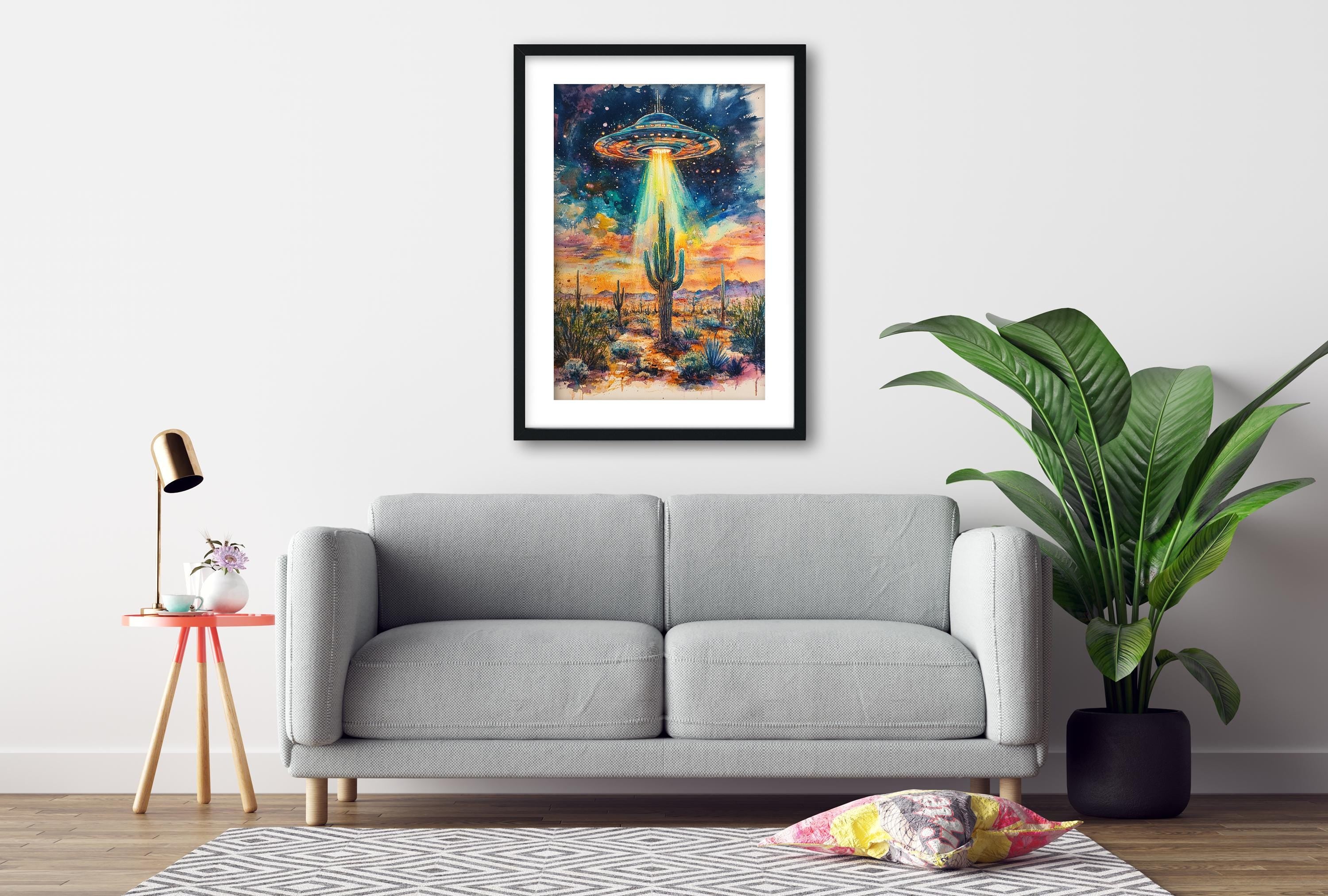 a gray sofa, a framed artwork of a cactus with an alien spacecraft hovering above it, and a potted plant on the floor.
