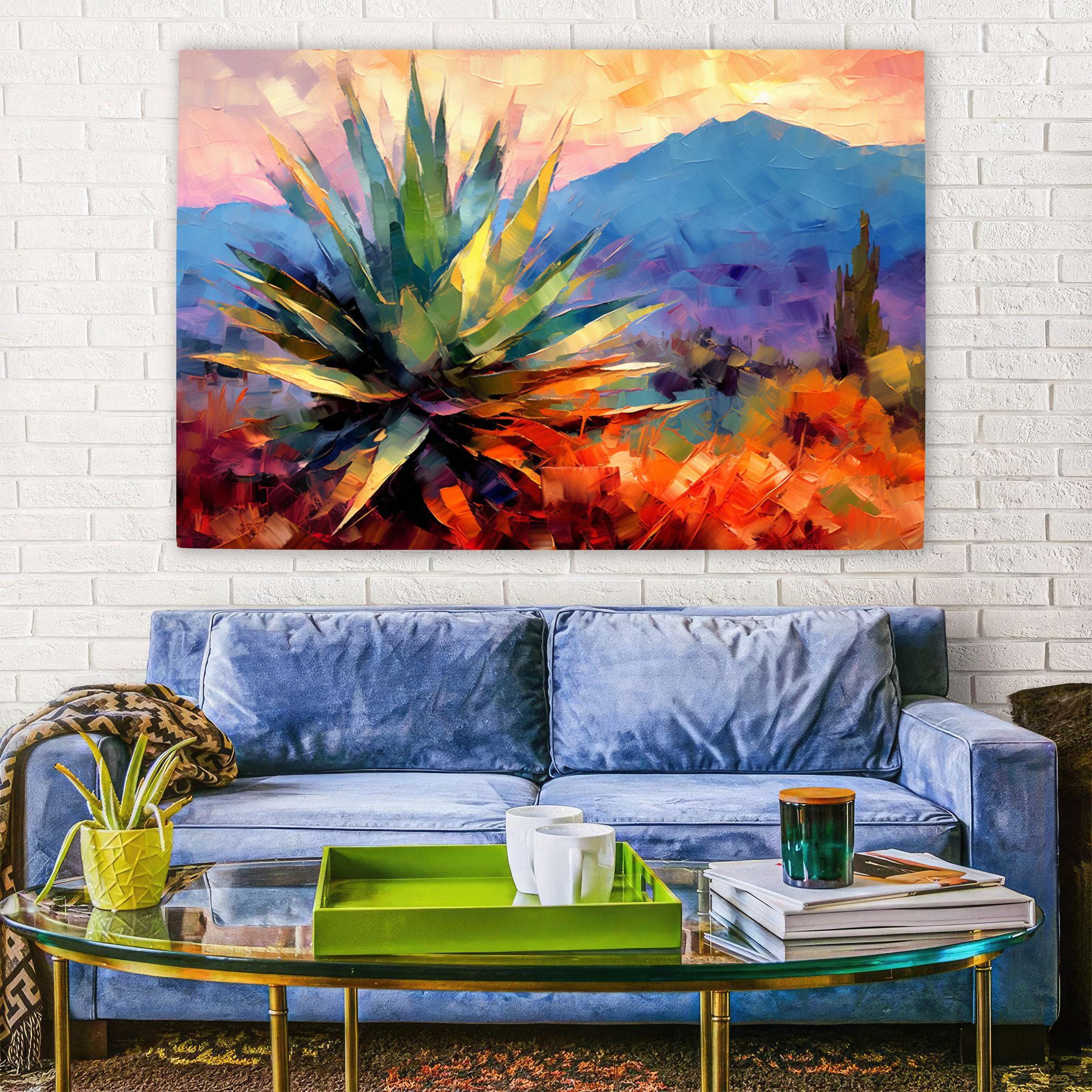 a vibrant painting of a desert landscape with a large cactus in the foreground, hanging on a white brick wall above a blue couch. The couch is positioned in front of a glass coffee table, which holds a few items such as a green tray, a cup, and a book.