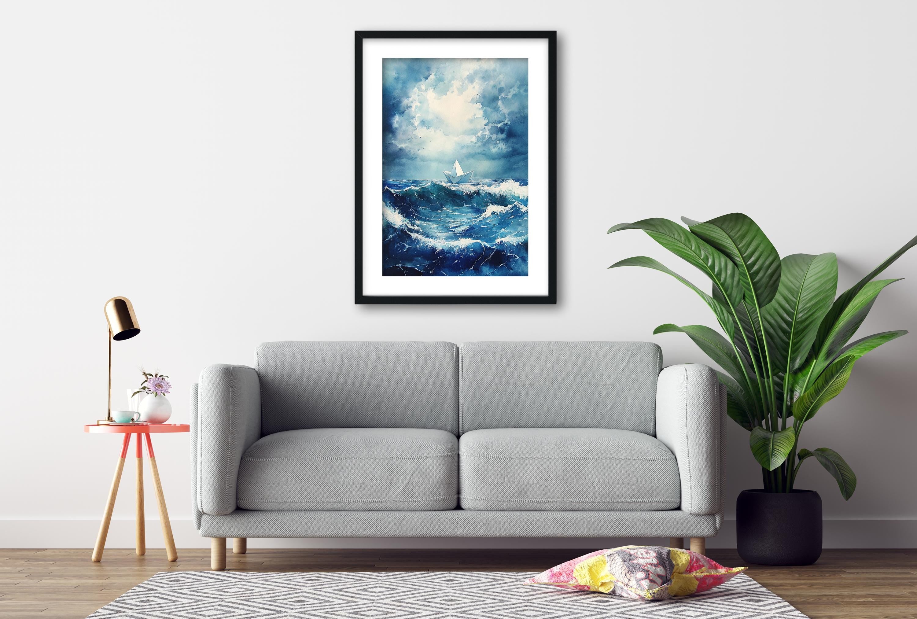 a gray sofa, a framed painting of a stormy ocean, a small table with a lamp, and a potted plant, all arranged in a living room setting.