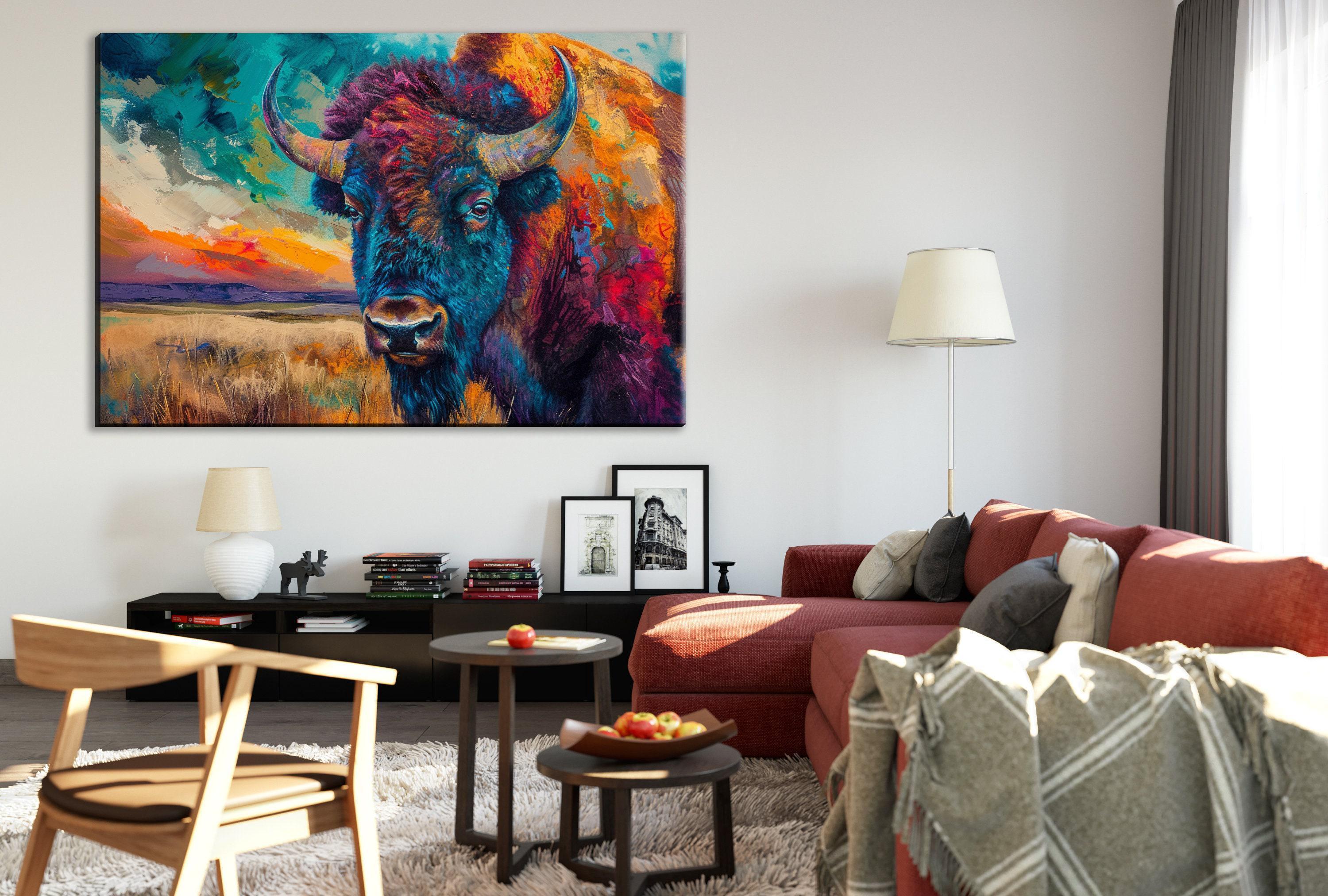 a living room with a large, colorful painting of a buffalo on the wall. The buffalo has vibrant colors and horns, creating a striking focal point in the room. The living room is furnished with a red couch, a wooden chair, and a coffee table. There are also several books and decorative items on the coffee table, adding to the cozy and inviting atmosphere of the space.