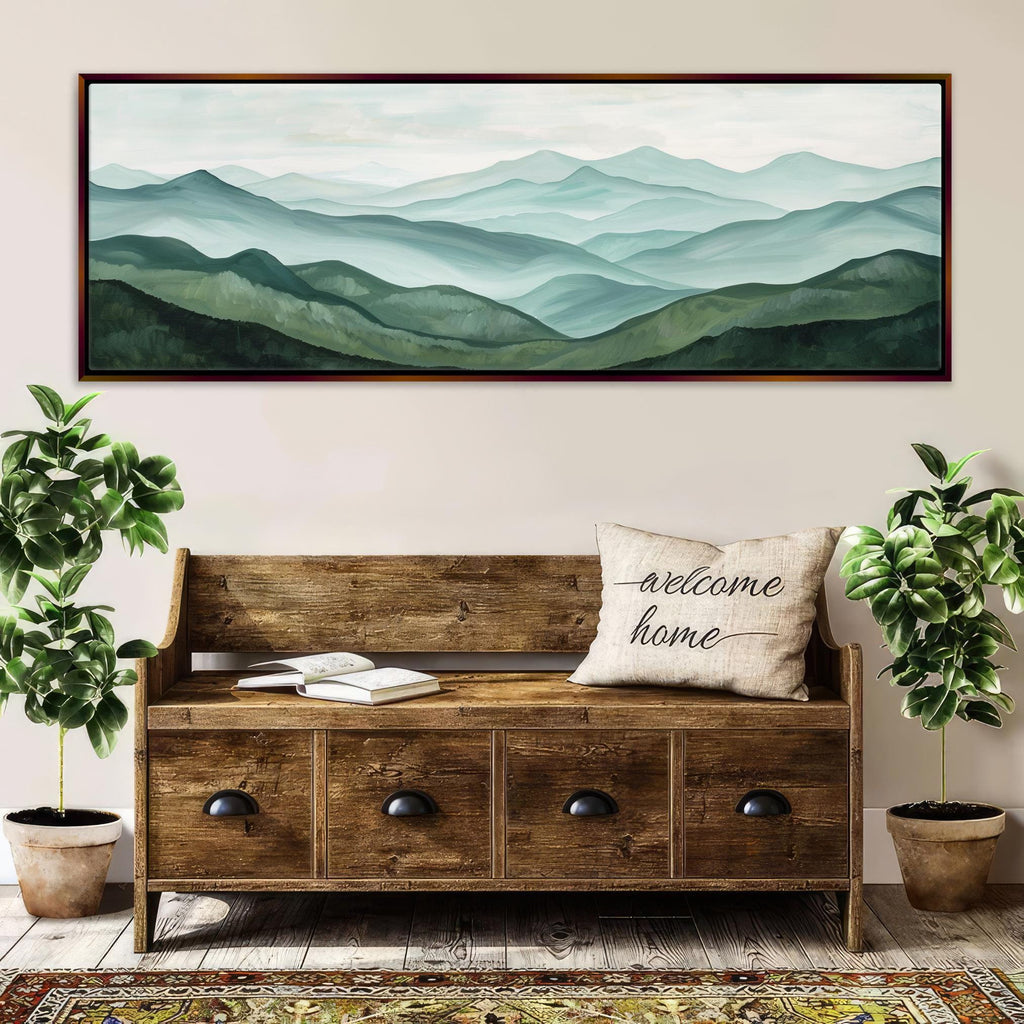a large wooden bench with a "welcome home" pillow, surrounded by potted plants and a framed landscape painting of a mountain range on the wall above it.