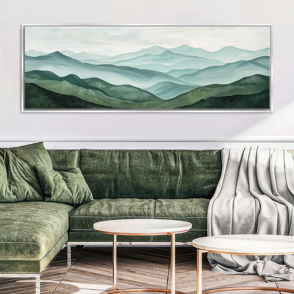 a living room with a large painting of a mountain landscape hanging on the wall above a green velvet sofa. The sofa is positioned in front of a round coffee table, and there is a white blanket draped over the arm of the sofa.