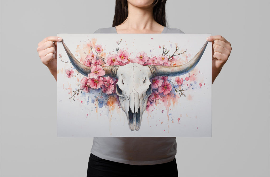 A woman holds up a framed print featuring a detailed illustration of a white skull with large horns, surrounded by pink flowers.
