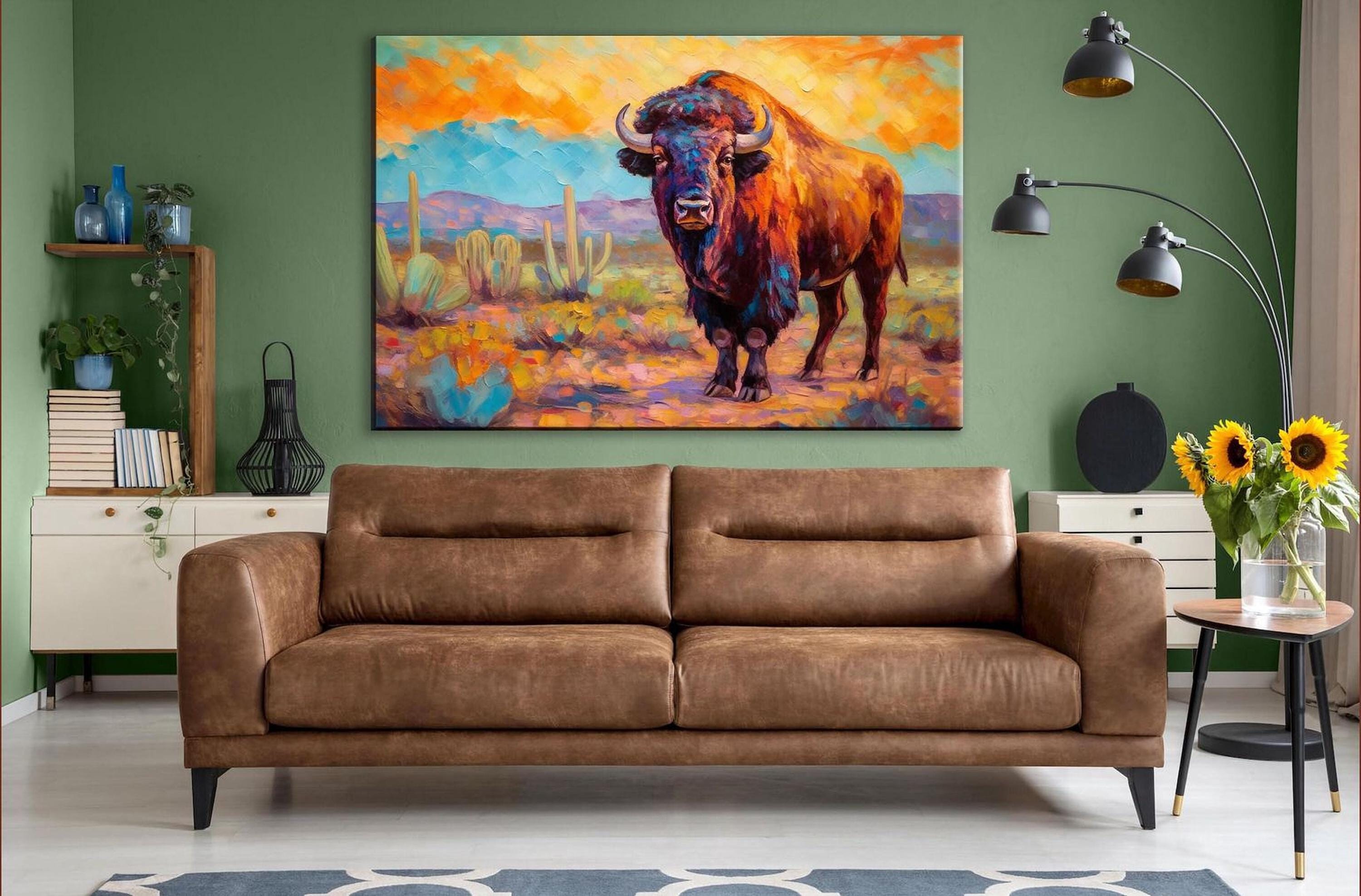 a large painting of a buffalo in a desert landscape, hanging on a green wall above a brown leather couch in a living room setting.