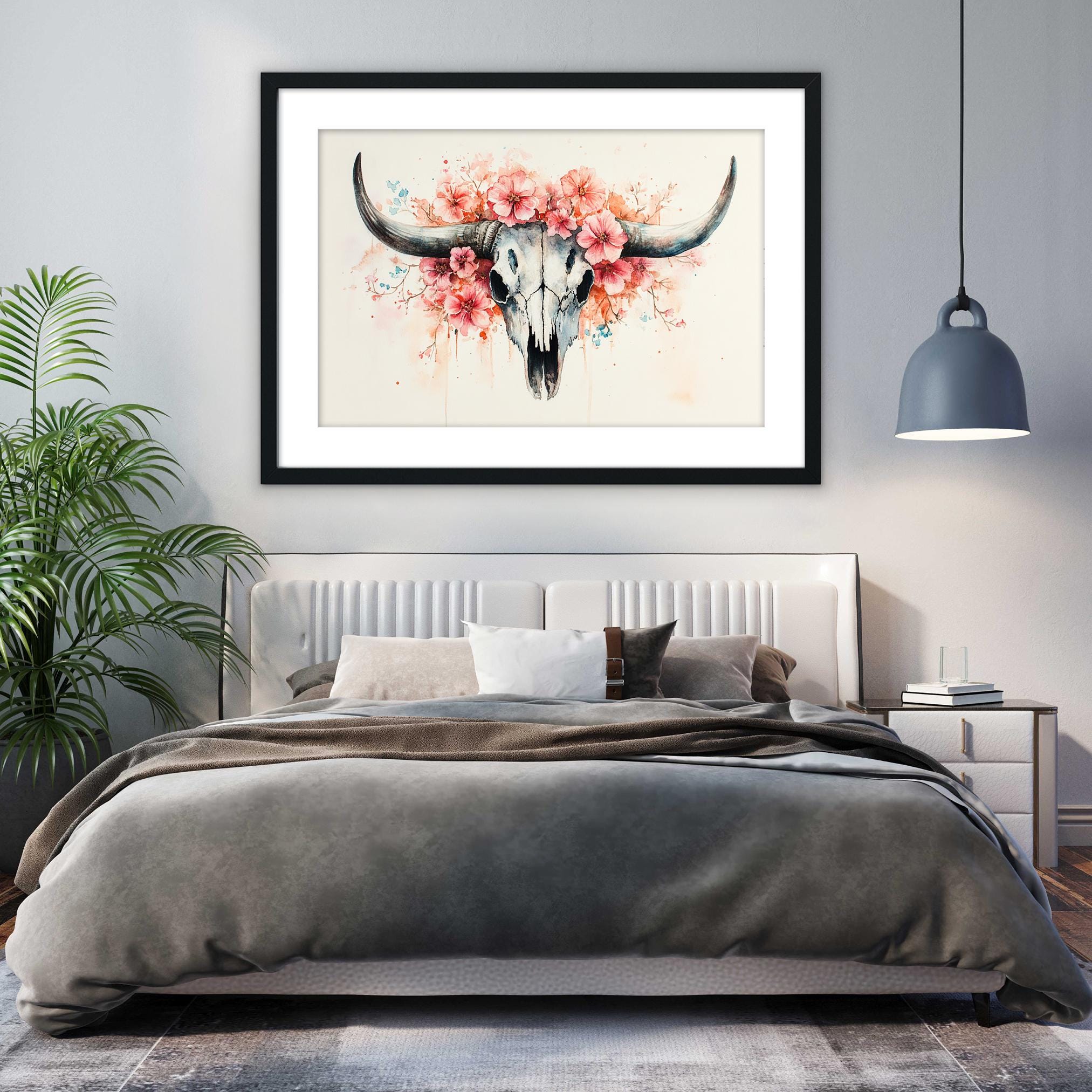 a bedroom with a large bed, a framed artwork of a skull with flowers hanging above it, and a potted plant to the left.