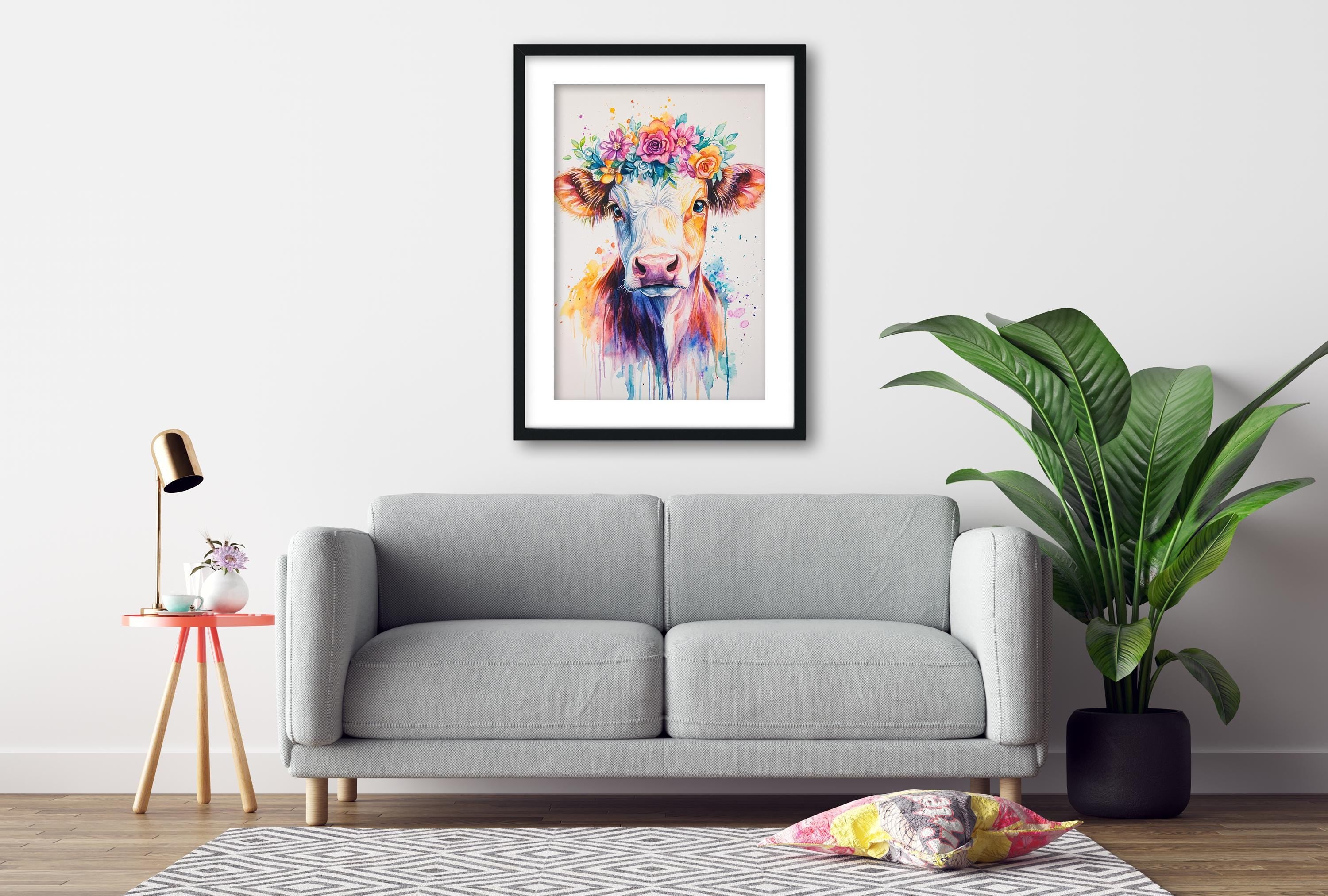 a gray sofa, a framed painting of a cow with a colorful flower crown, a small table with a lamp, and a potted plant, all arranged in a cozy living room setting.
