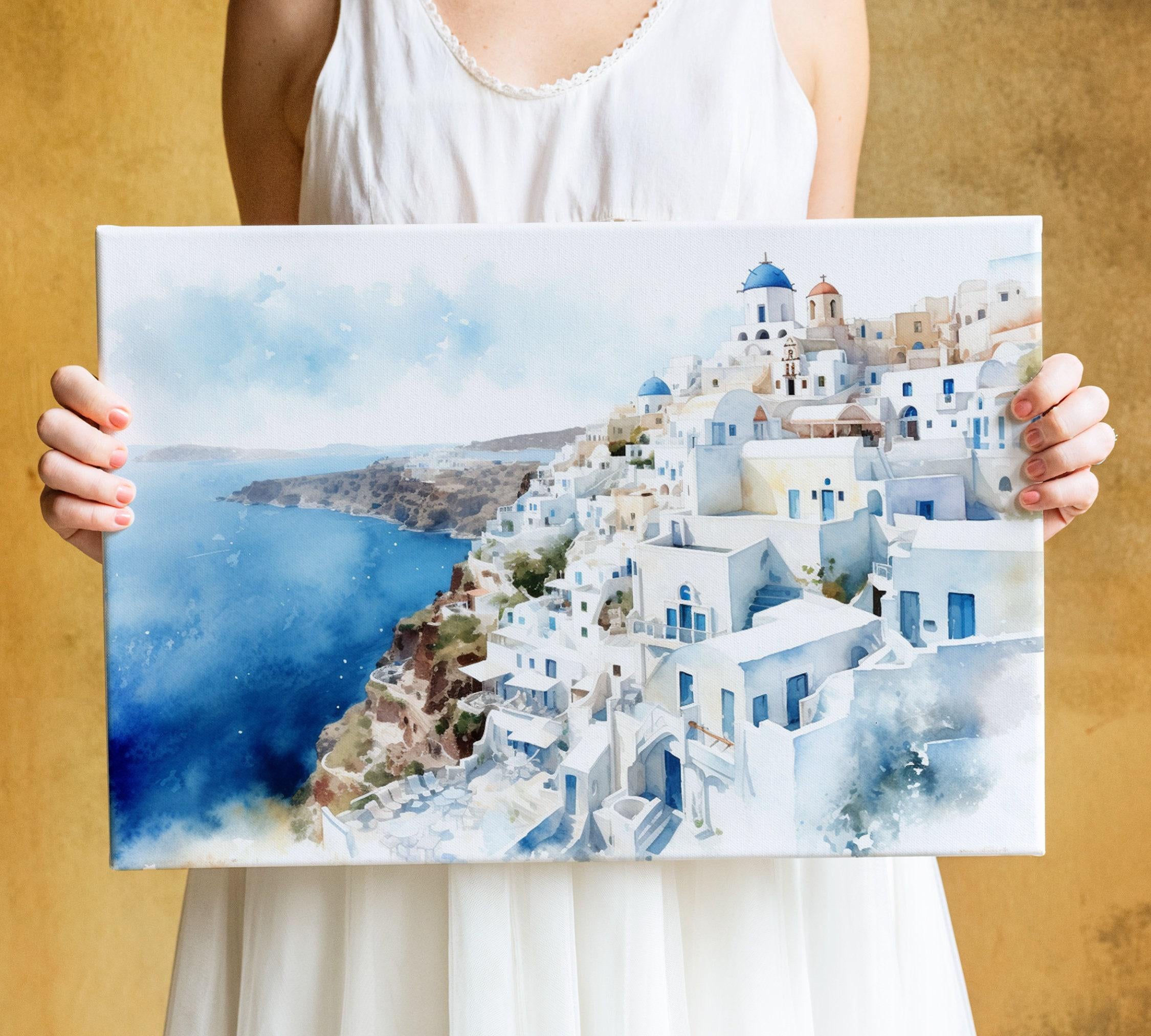 A woman holds a framed painting of a picturesque coastal town with white buildings and blue roofs, overlooking the ocean.