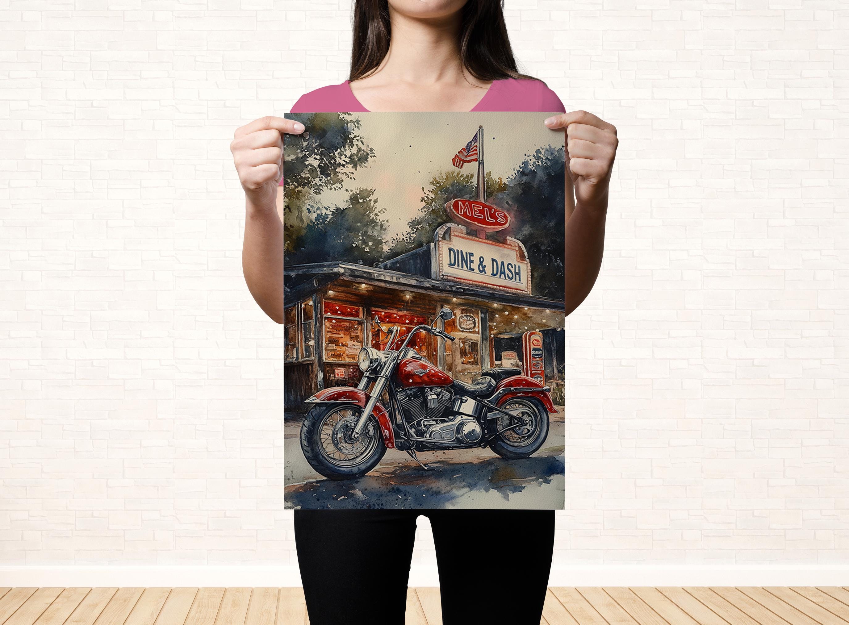 A woman holds up a framed print of a red motorcycle parked in front of a diner with a sign that reads "Dine & Dash".
