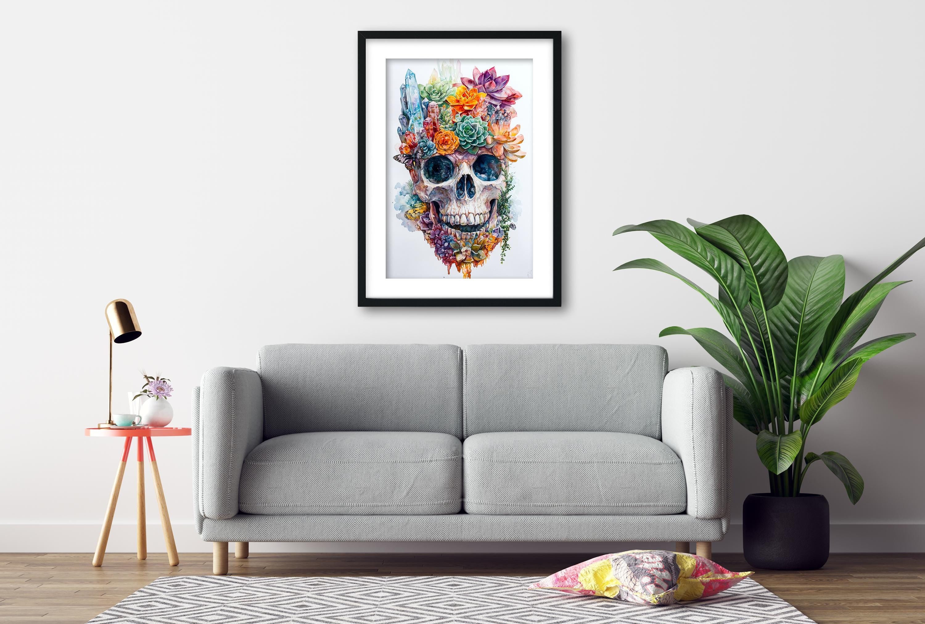 a gray sofa, a framed artwork of a colorful skull, a small table with a lamp, and a potted plant, all arranged in a living room setting.