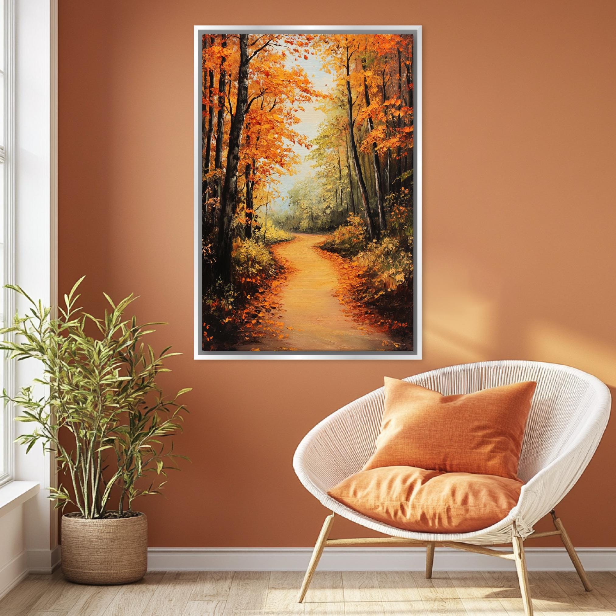 a cozy living room with a large painting of a forest path in autumn hanging on the wall. The painting is framed and has a warm orange and yellow color scheme. The room is furnished with a white wicker chair and a potted plant, creating a comfortable and inviting atmosphere.