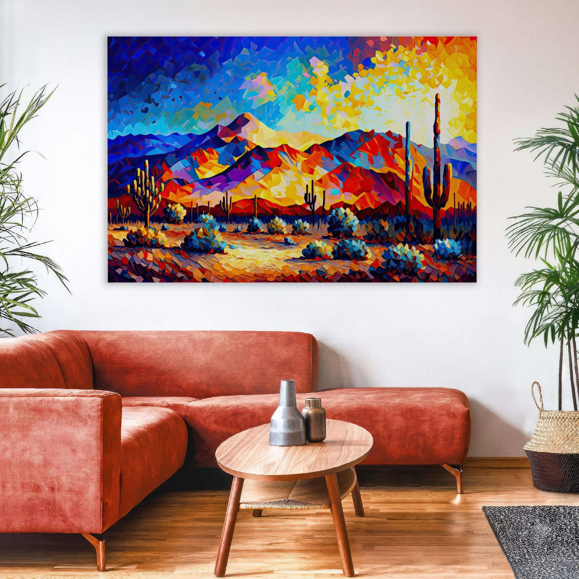 a vibrant desert landscape painting hanging on a wall above a cozy living room setting with a red sofa, a wooden coffee table, and a potted plant.