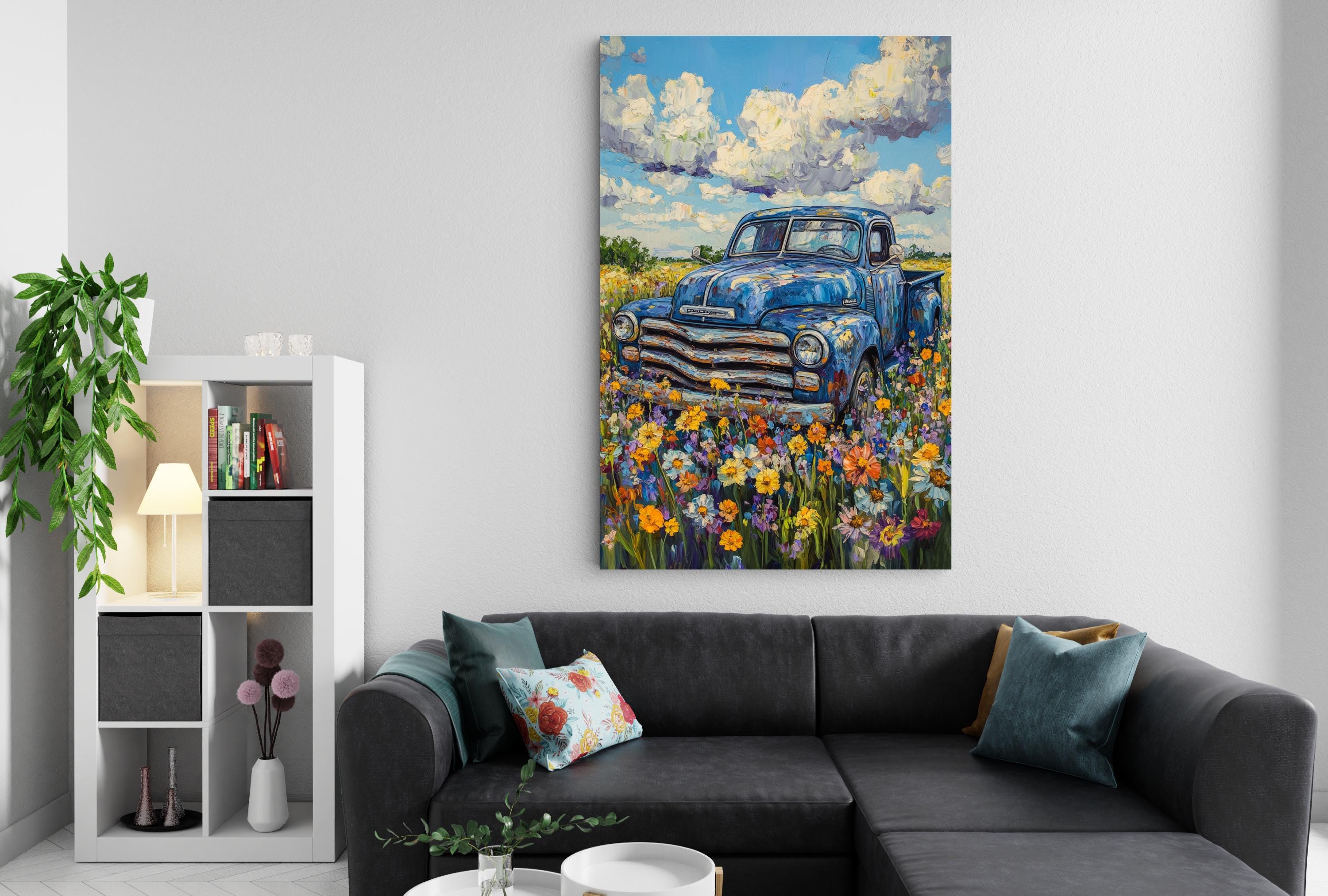 a large painting of a blue truck parked in a field of colorful flowers, hanging on a wall above a black couch with throw pillows.