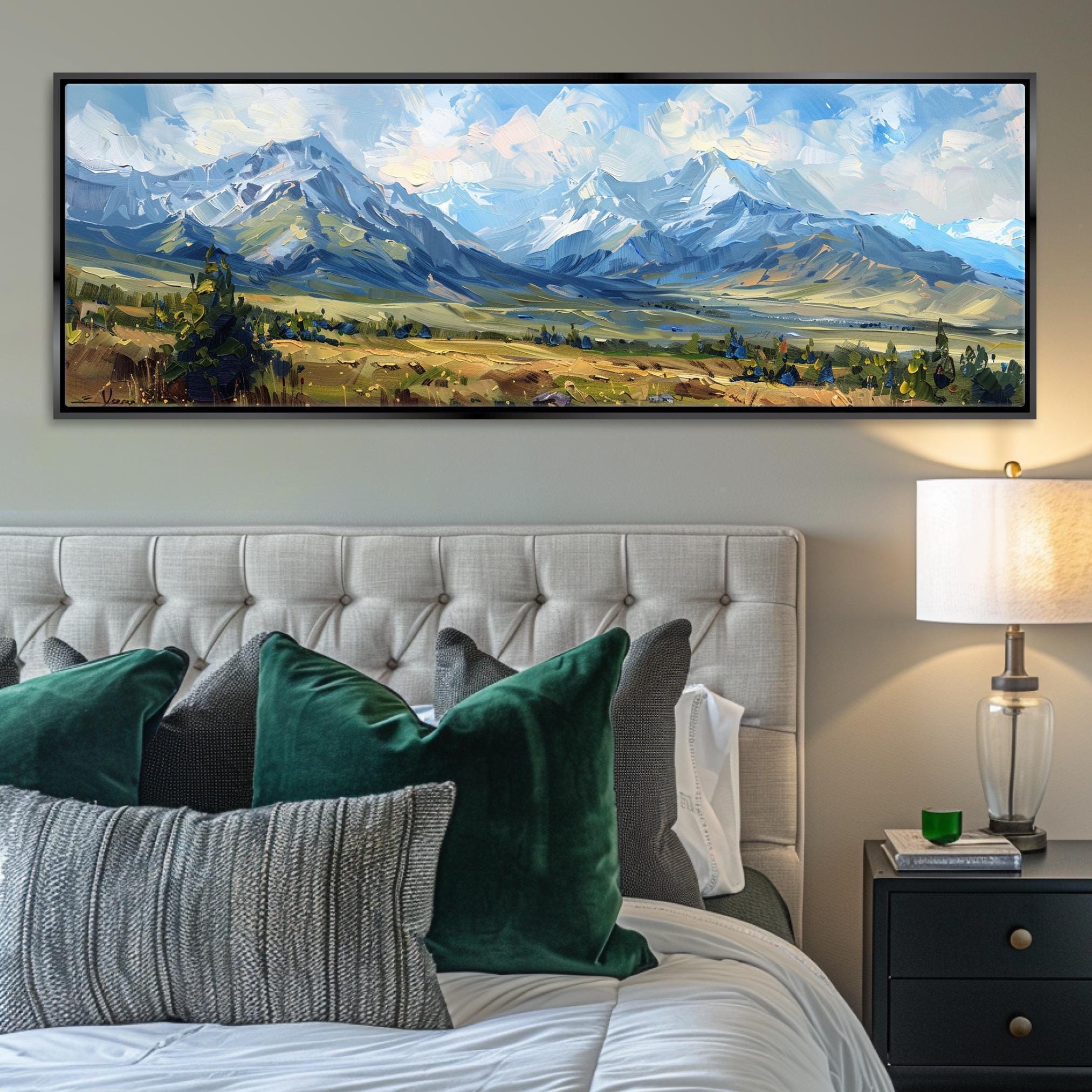 a large landscape painting hanging on a wall above a bed with white tufted headboard. The painting depicts a scenic mountain range with a cloudy sky.