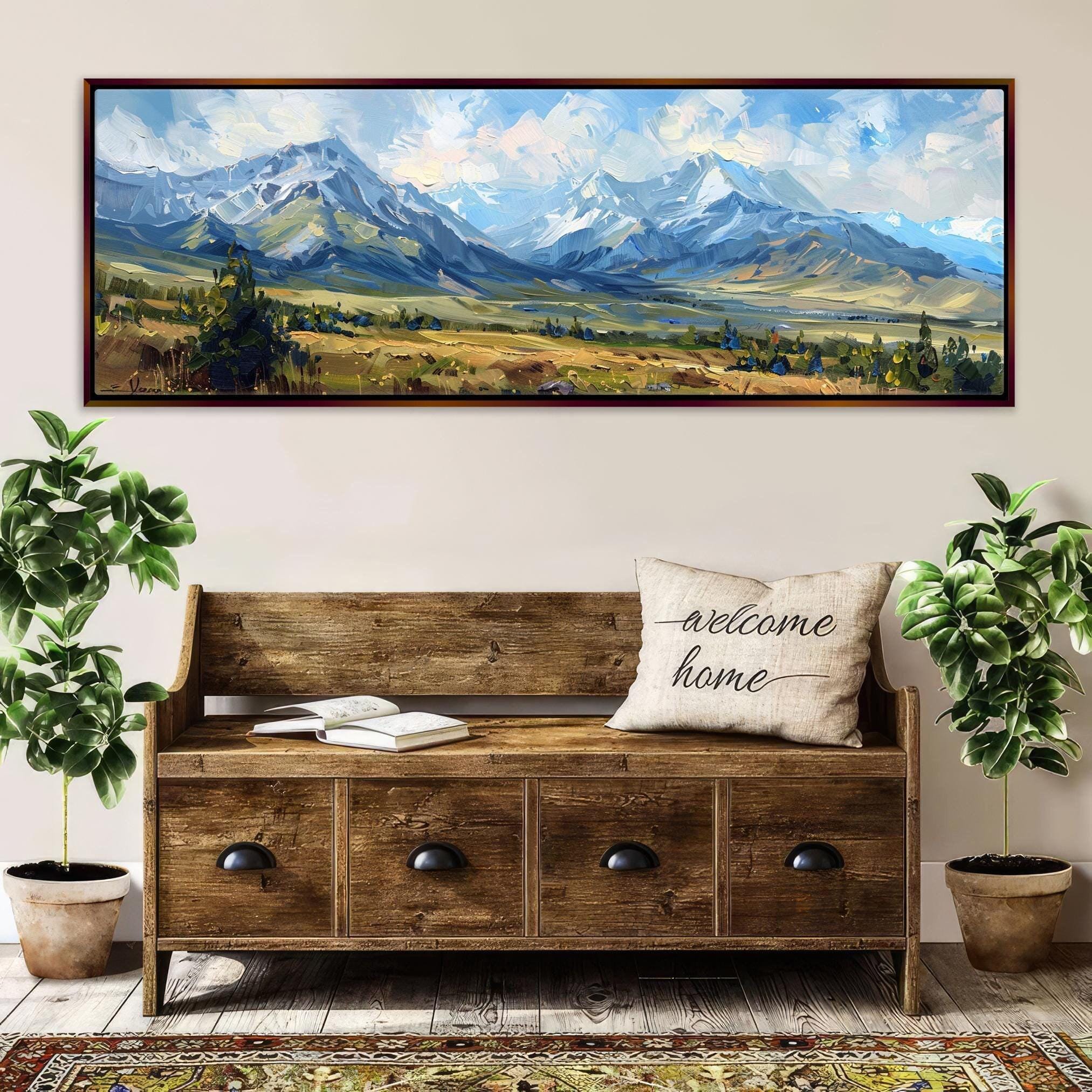 a large wooden bench with a "welcome home" pillow, surrounded by potted plants and a framed landscape painting depicting a mountainous, forested area.