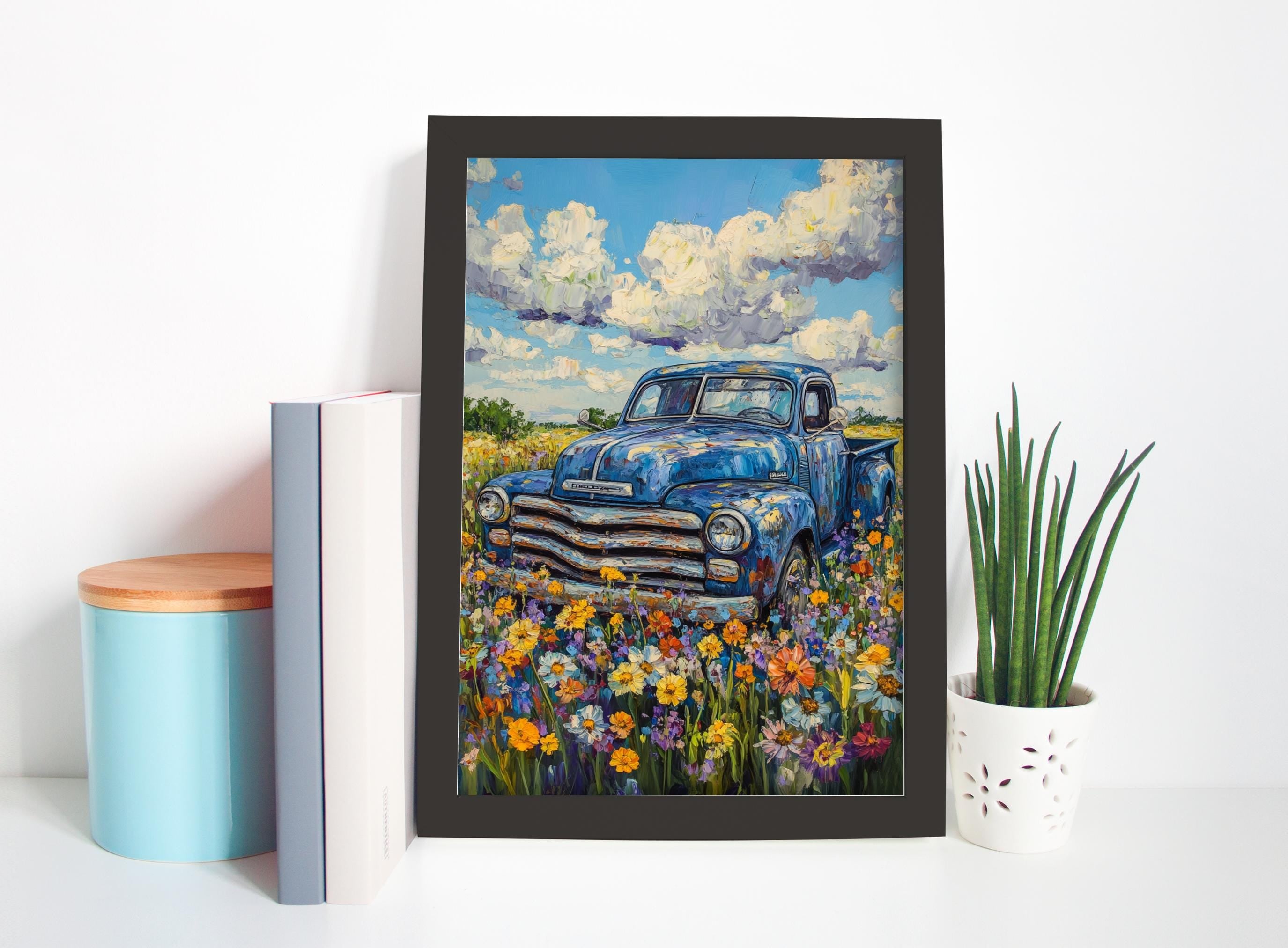 a framed painting of an old blue truck parked in a field of colorful flowers, with a cloudy sky in the background.