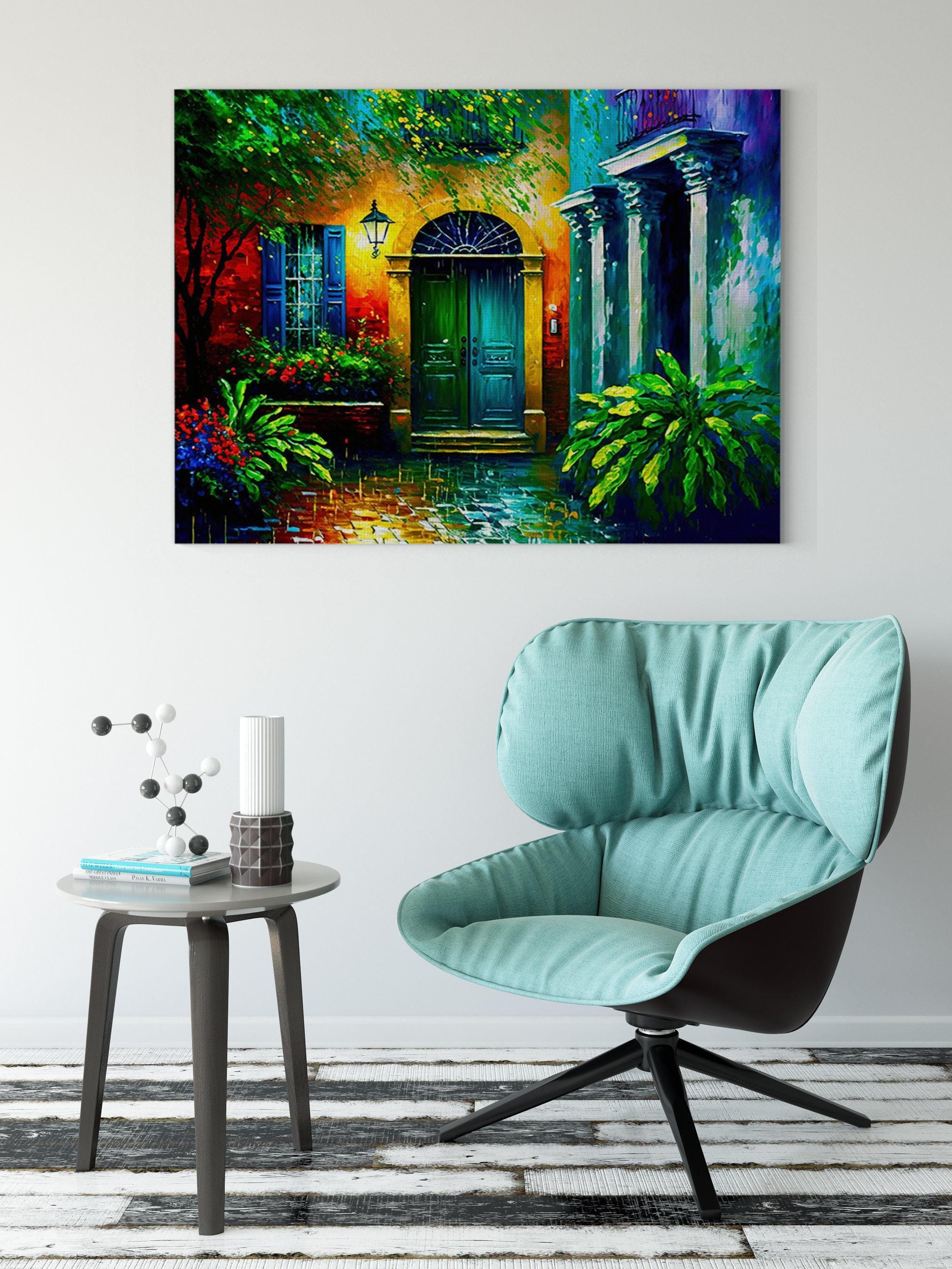 a vibrant painting of a colorful house with a green door, set against a backdrop of lush greenery and flowers. The painting is hung on a white wall above a modern chair and a small side table, creating a cozy and inviting atmosphere in the room.