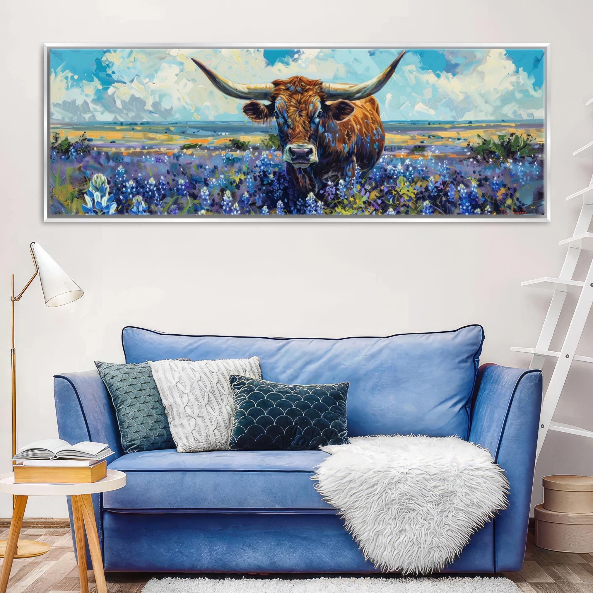 a large painting of a bull with horns, set against a field of flowers, hanging on a wall above a blue couch with pillows.