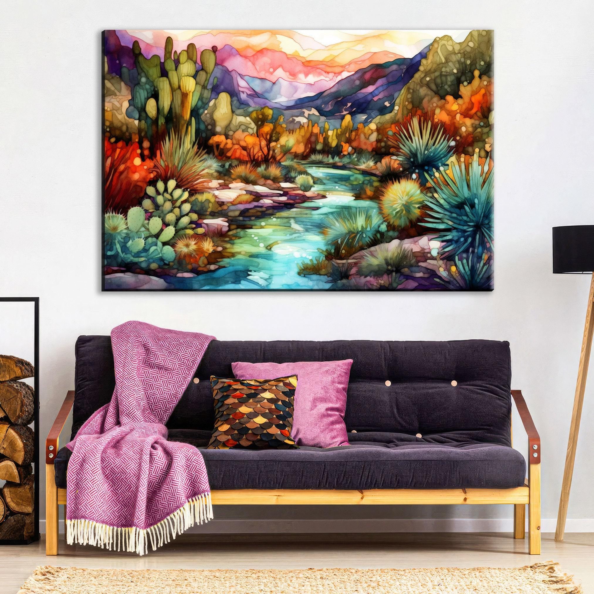 a vibrant, colorful painting of a desert landscape with mountains, cacti, and a winding river. The painting is hung on a wall above a black couch with colorful throw pillows.