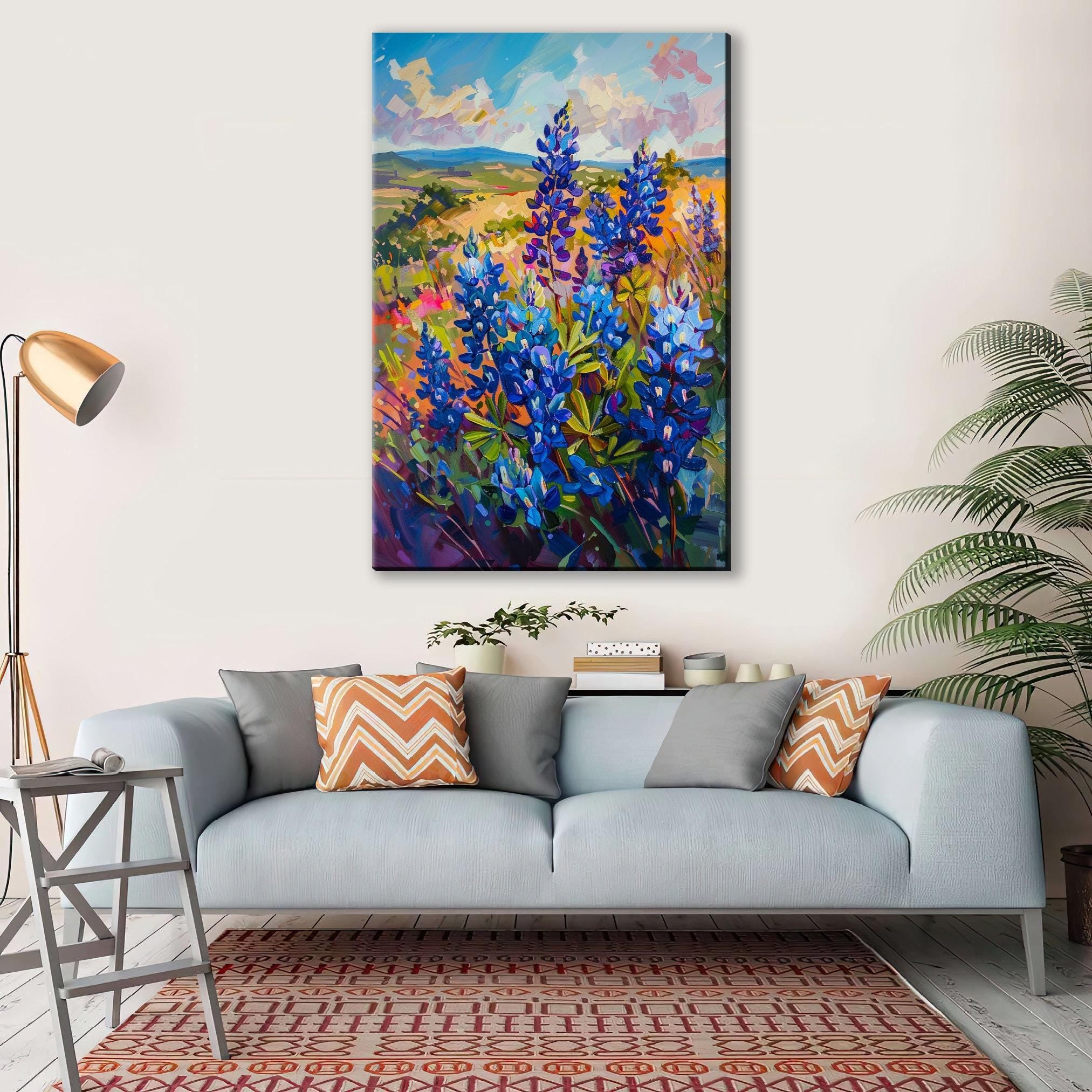 a large painting of a field of blue flowers hanging on a wall above a gray couch with orange and gray throw pillows.