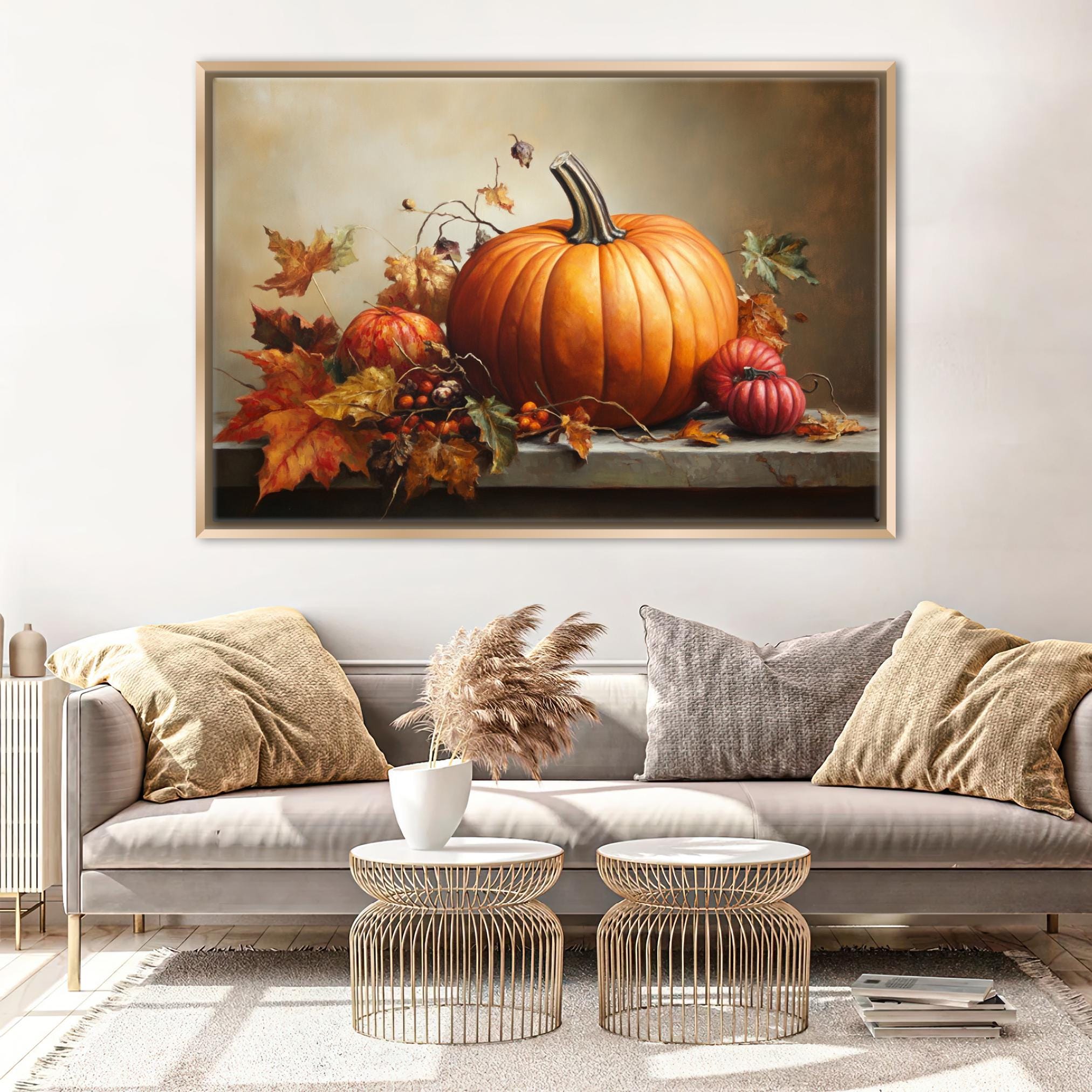 a large painting of a pumpkin and autumn leaves hanging on a wall above a gray sofa with two round coffee tables in front of it.