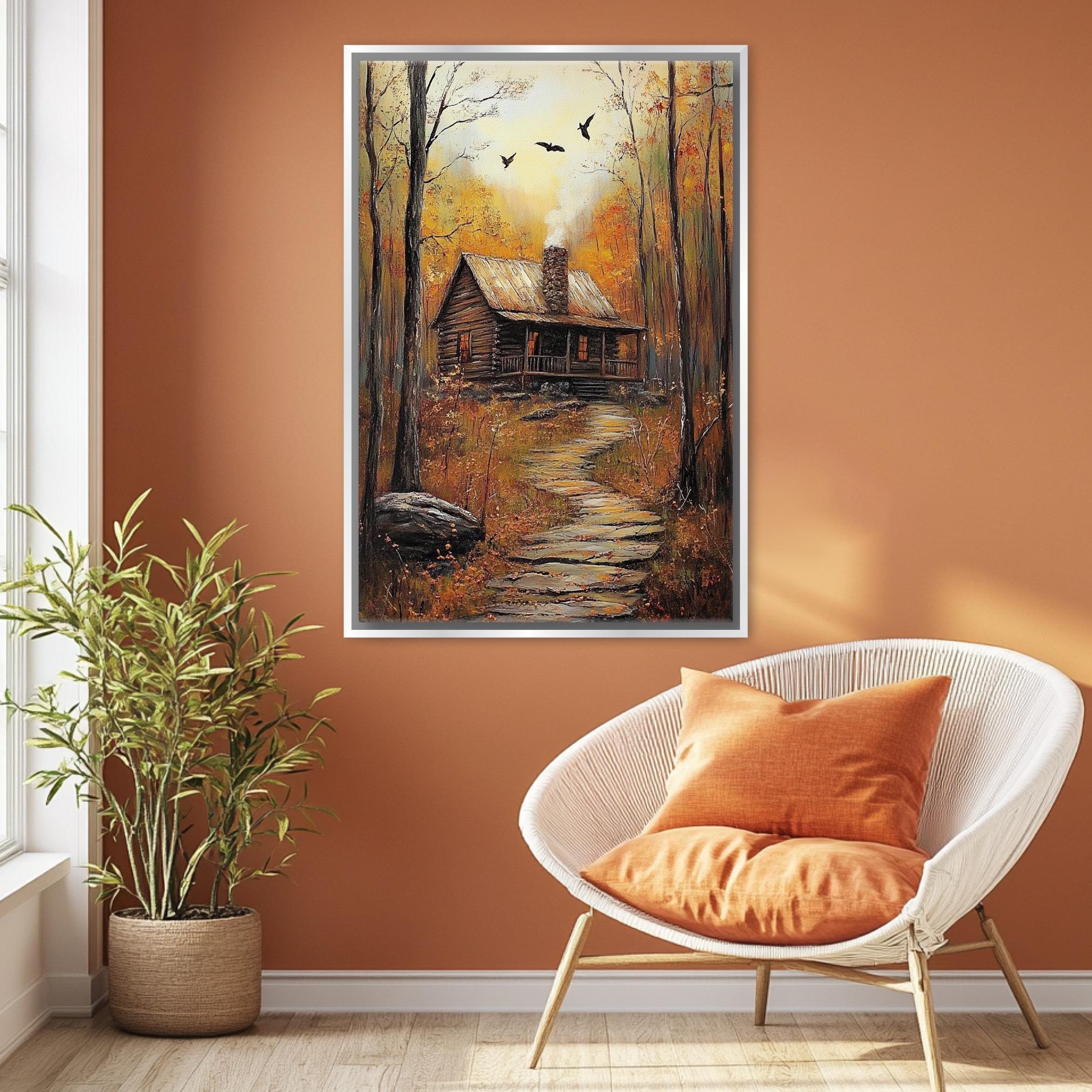 a cozy cabin nestled in a forest, with a path leading up to it. The cabin is surrounded by trees and foliage, creating a serene and peaceful atmosphere. The painting is hung on a wall above a white wicker chair, which is positioned in front of a potted plant. The overall scene conveys a sense of tranquility and harmony with nature.