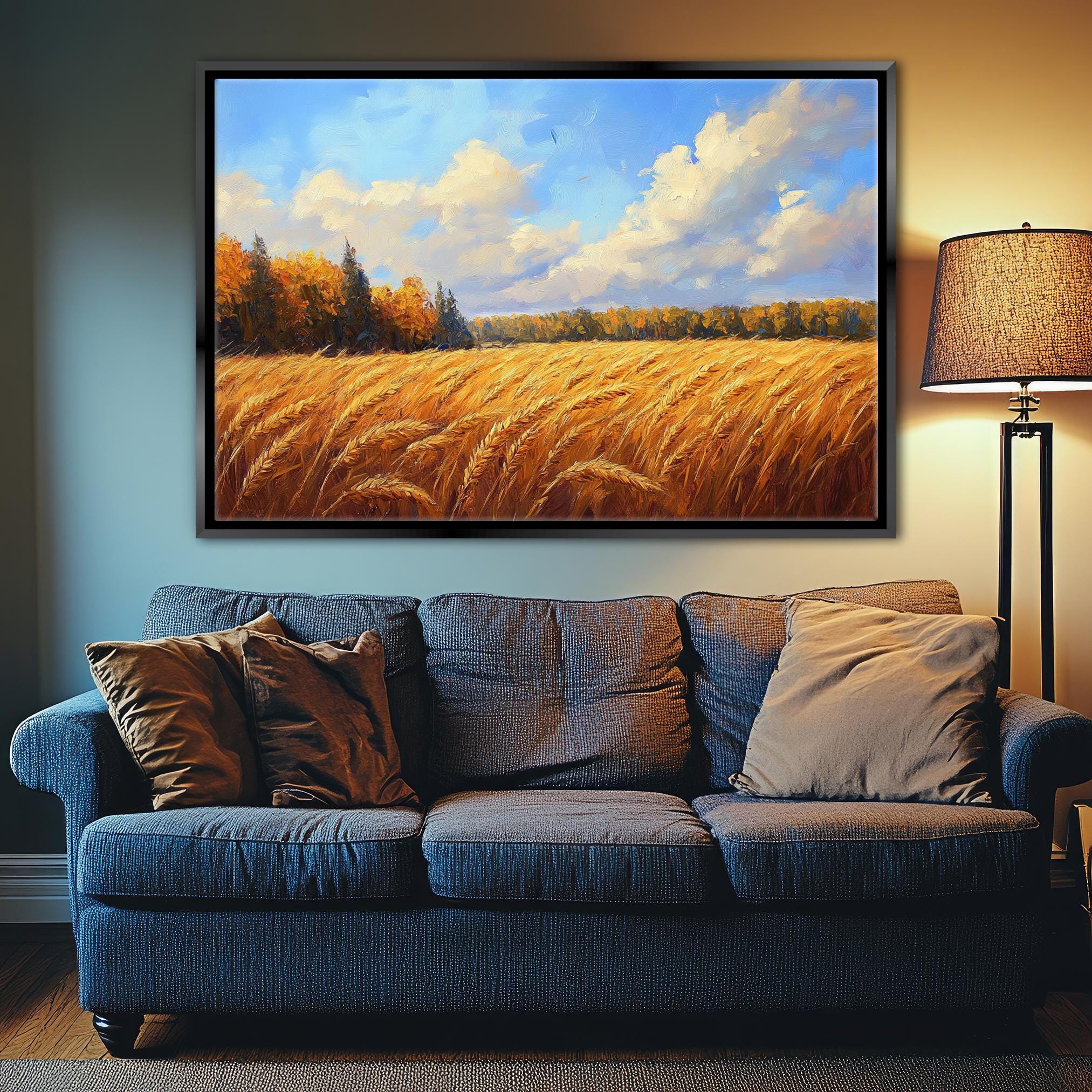 a large painting of a field of golden wheat hanging on a wall above a blue couch with pillows.