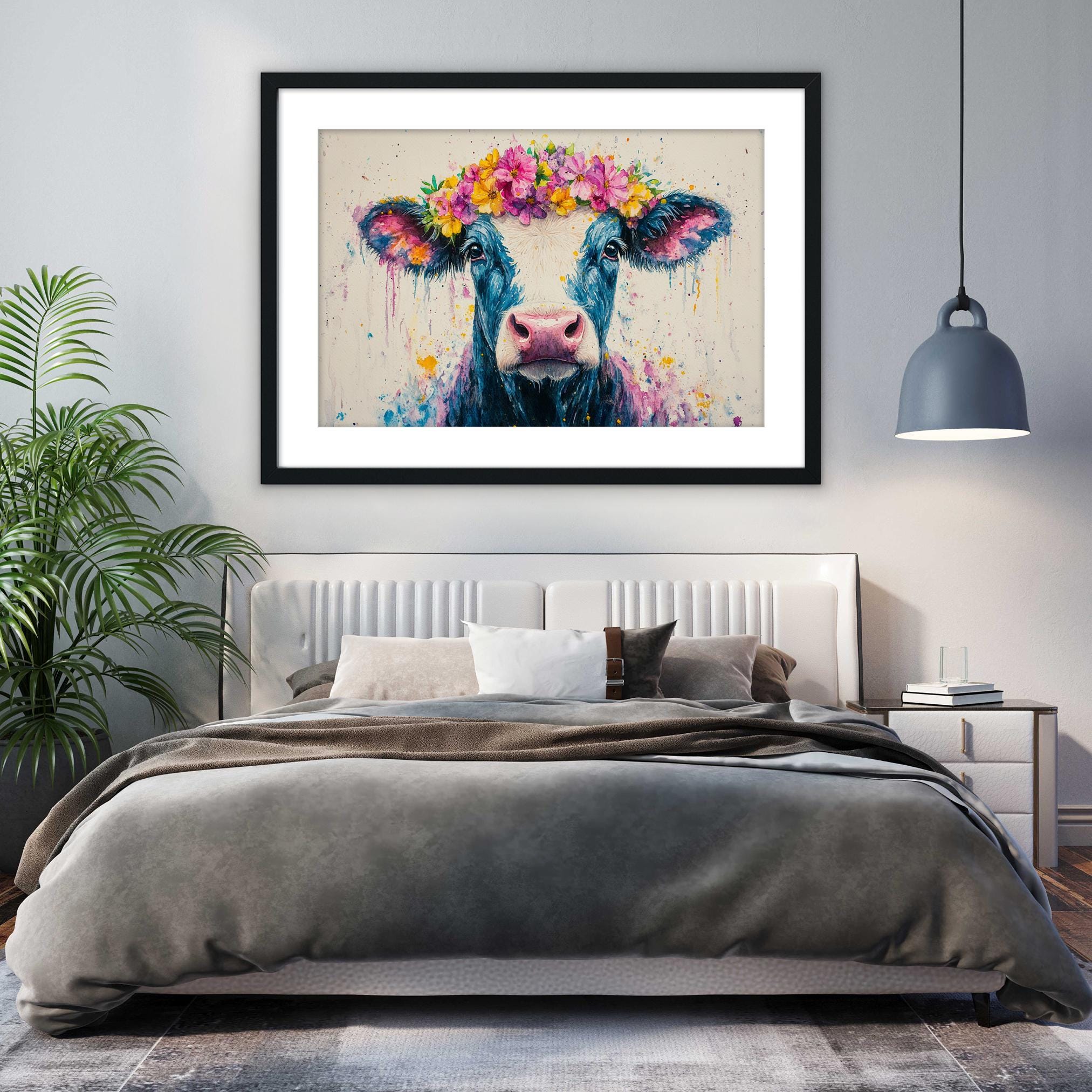 a bedroom with a large bed, a framed painting of a cow with a flower crown on its head, and a potted plant on the left side of the room.