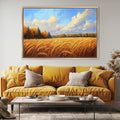 a large painting of a field of golden wheat against a blue sky with clouds, hanging on a wall above a yellow sofa with two pillows.