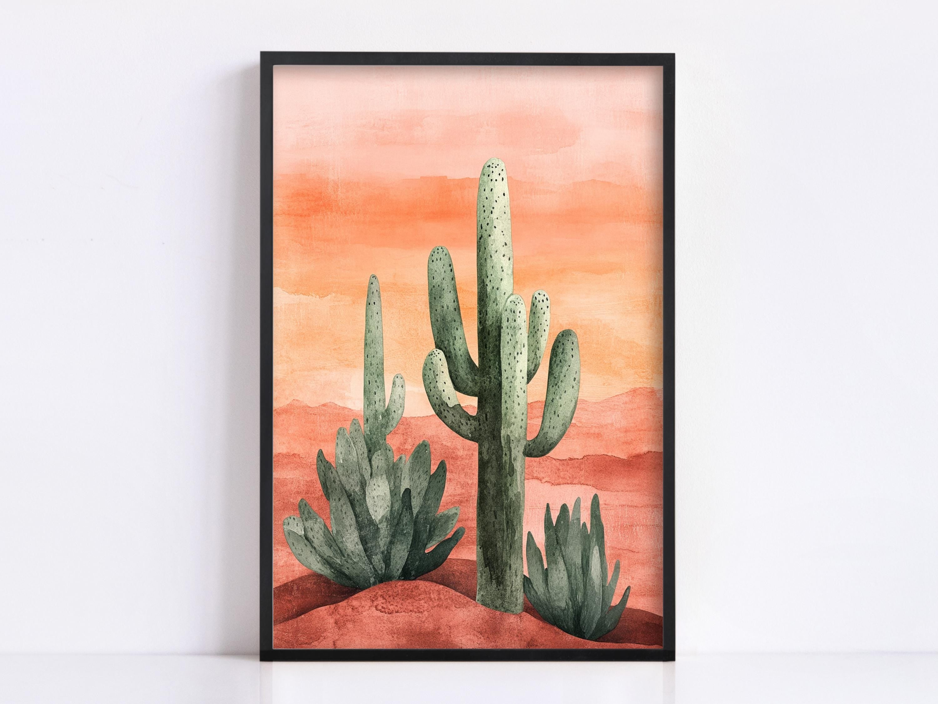 A framed watercolor painting depicting a desert landscape with three cacti against a warm, orange-red background.
