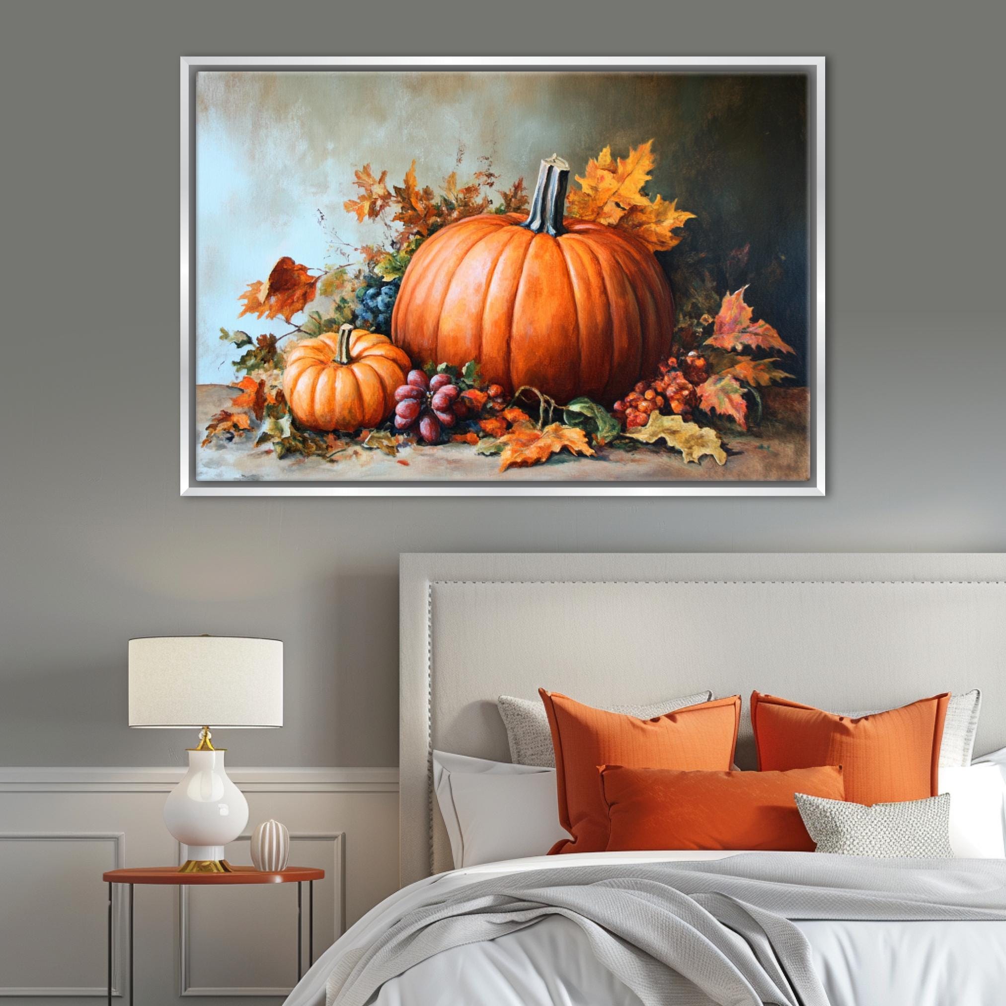 a large framed painting of a pumpkin and autumn leaves on a wall above a bed with orange pillows and a white headboard.