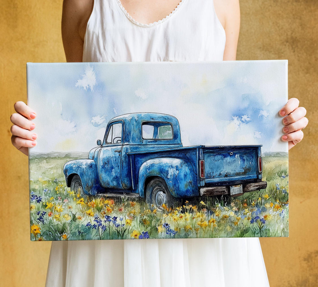 A woman holds a painting of an old blue pickup truck in a field of flowers.