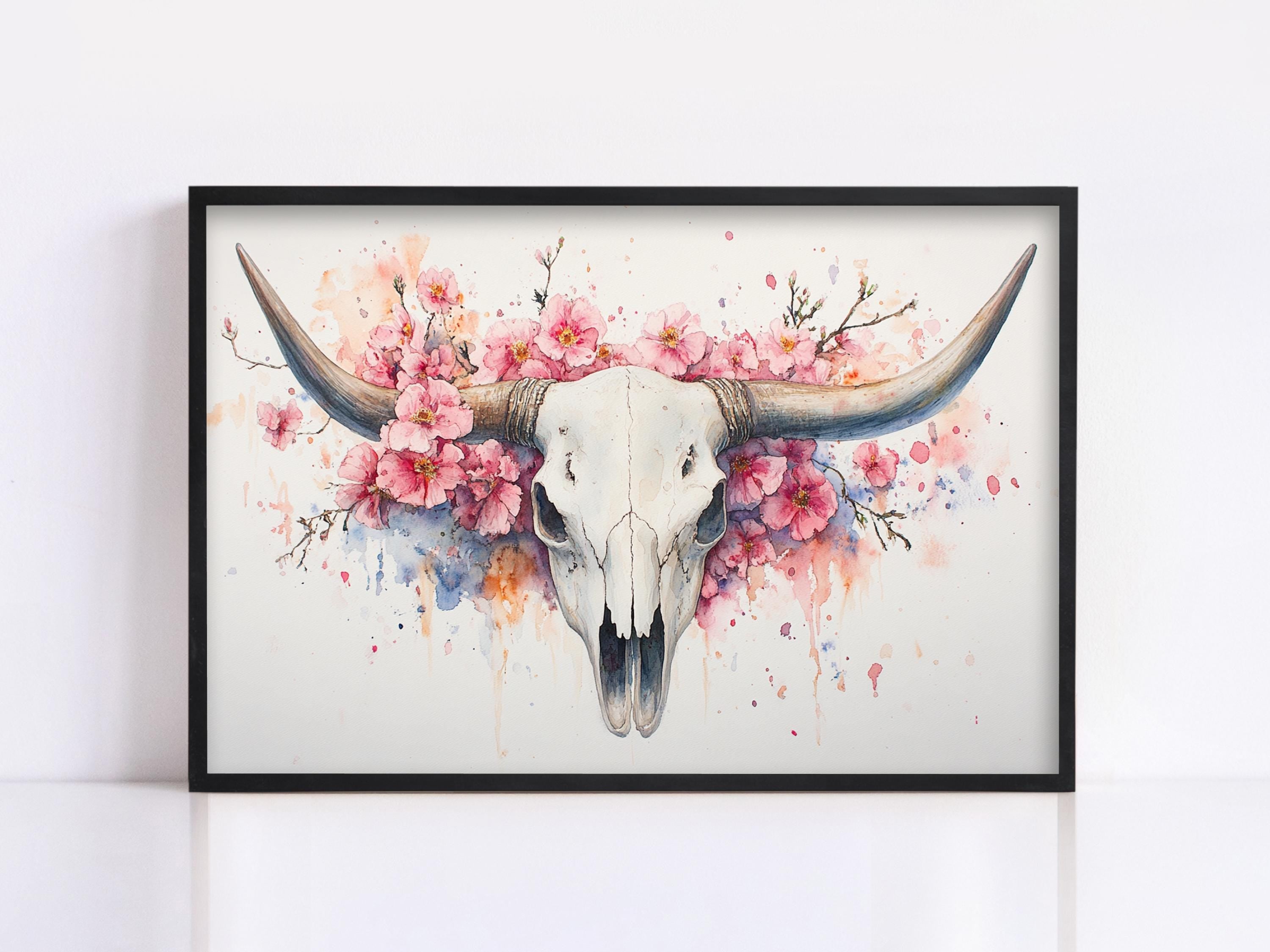 A framed painting depicting a white skull with large horns surrounded by pink flowers.