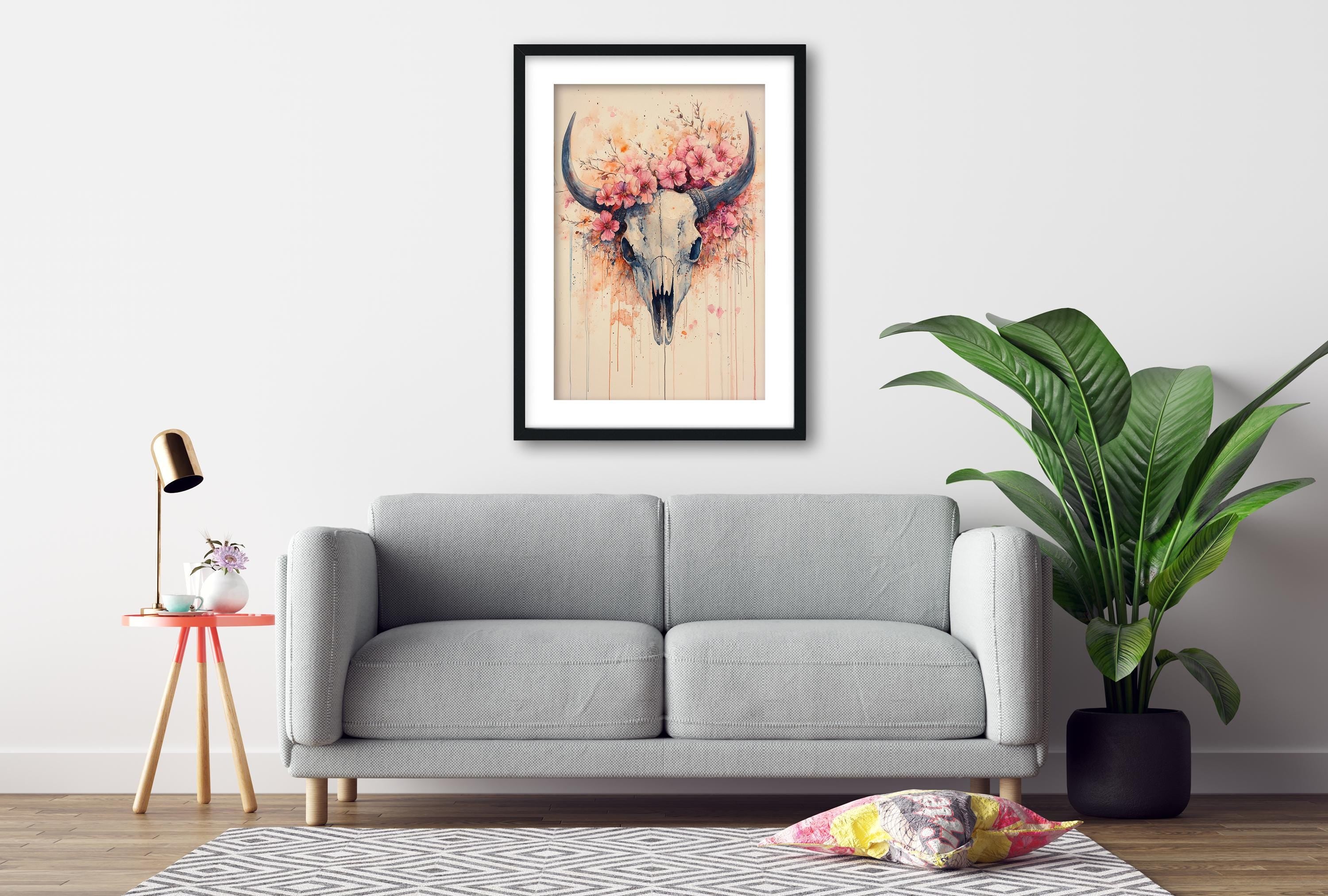 a gray sofa, a framed artwork of a skull with flowers, a small table with a lamp, and a potted plant, all arranged in a living room setting.