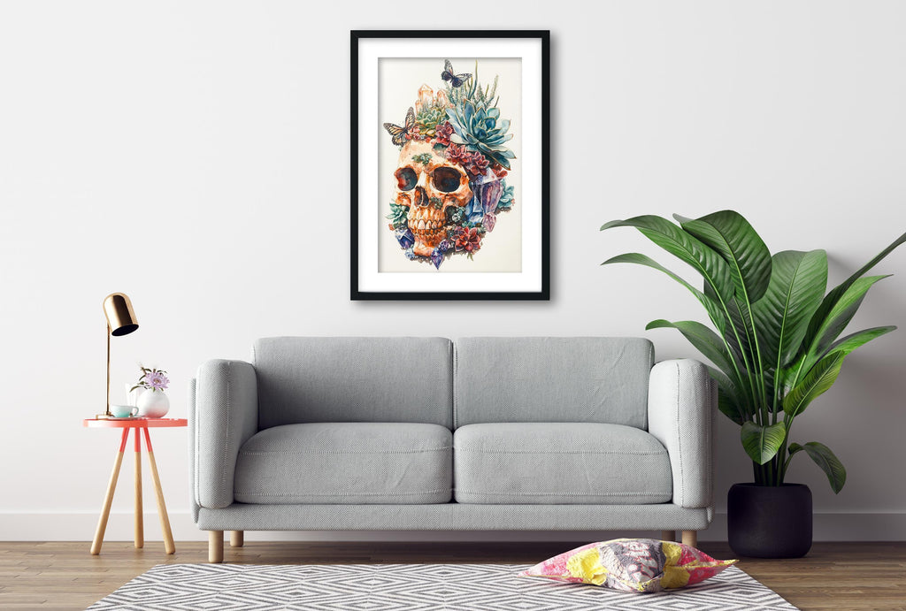 a gray sofa, a framed artwork of a skull with a floral design, a small table with a lamp, and a potted plant, all arranged in a living room setting.