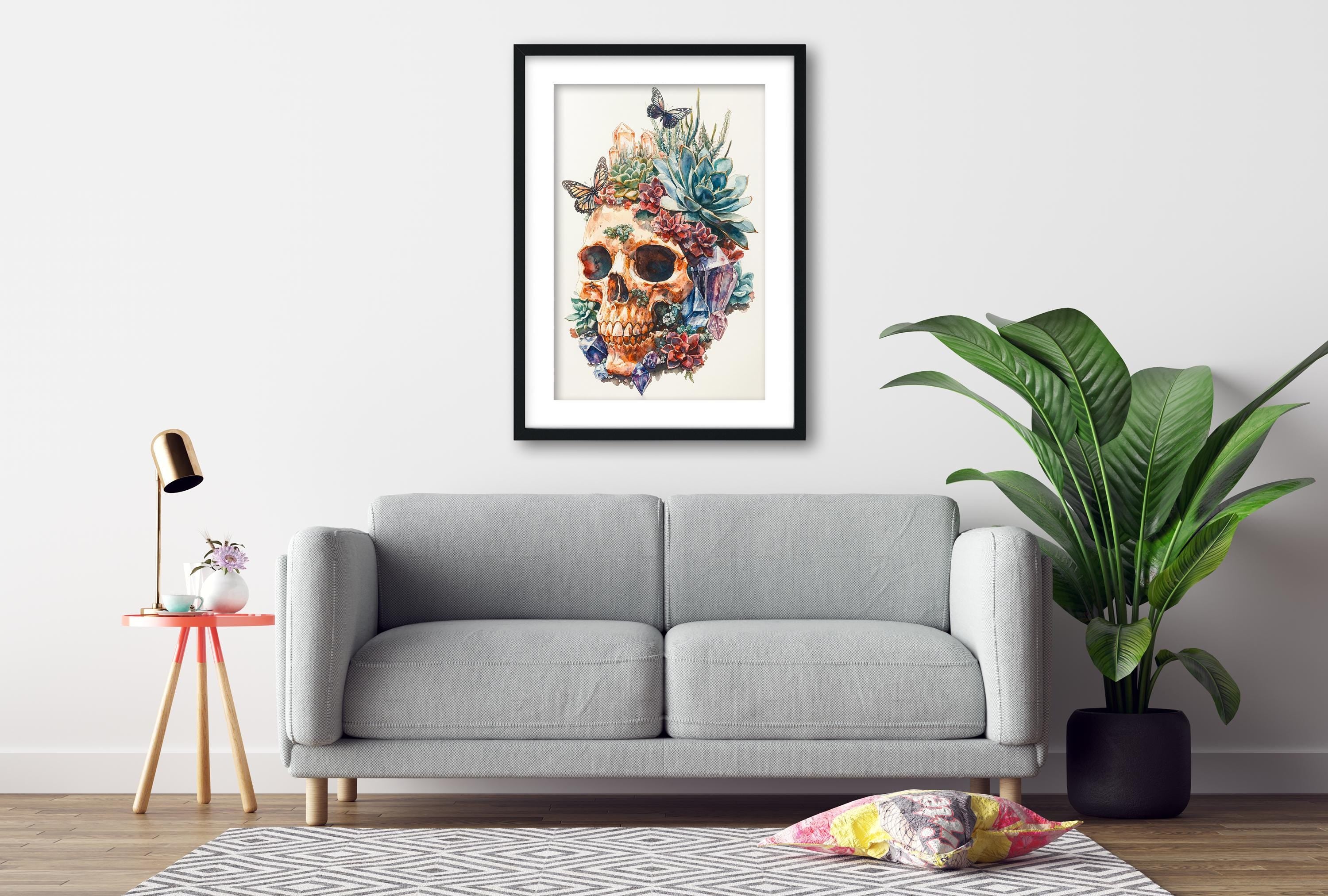 a gray sofa, a framed artwork of a skull with a floral design, a small table with a lamp, and a potted plant, all arranged in a living room setting.