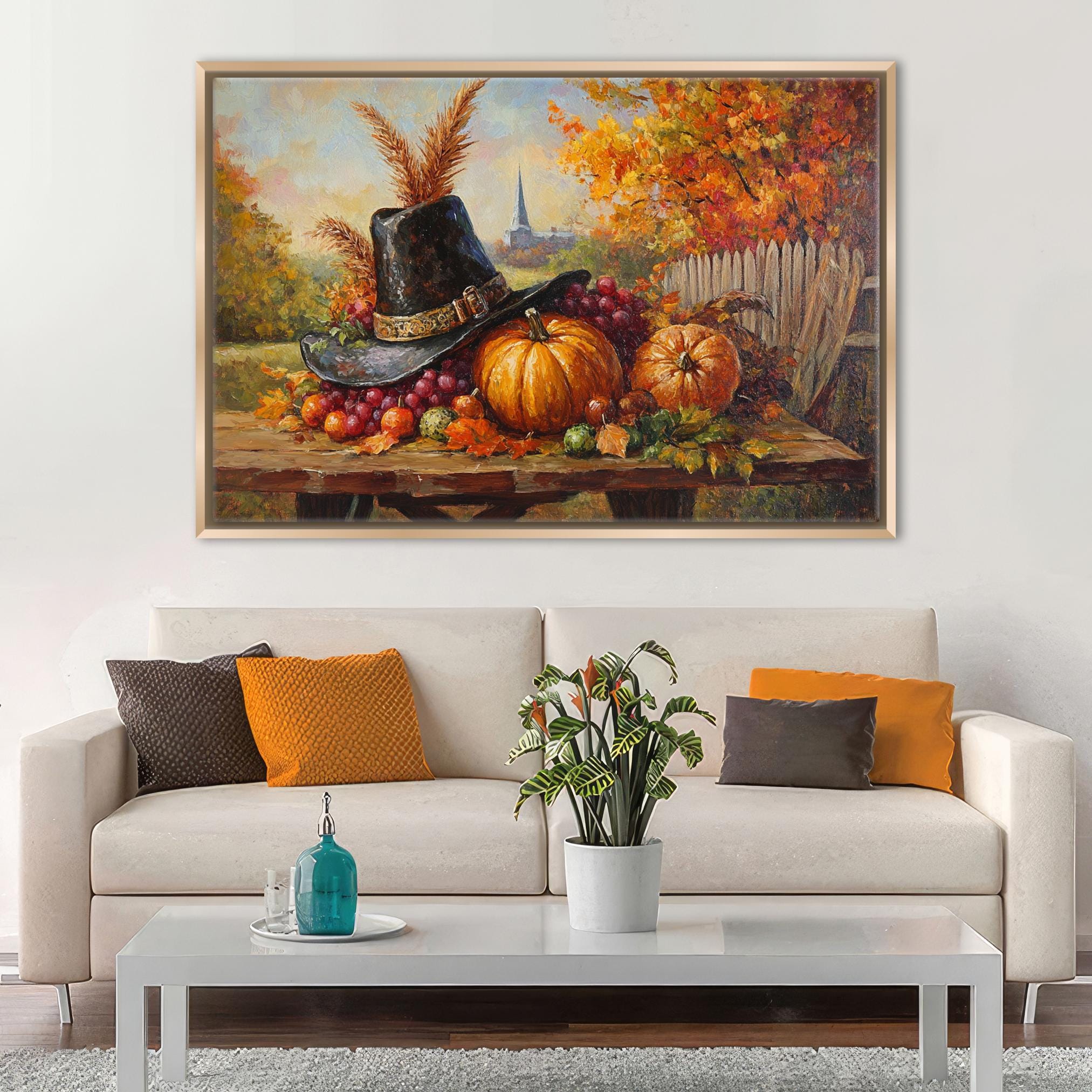 a cozy living room with a white sofa adorned with orange and brown throw pillows. Above the sofa, a large painting of a table with a hat, pumpkins, and other fall fruits and vegetables is displayed on the wall. The painting is framed in a gold frame, adding a touch of elegance to the room. In front of the sofa, there is a coffee table with a blue vase and a plant, contributing to the warm and inviting atmosphere of the space.