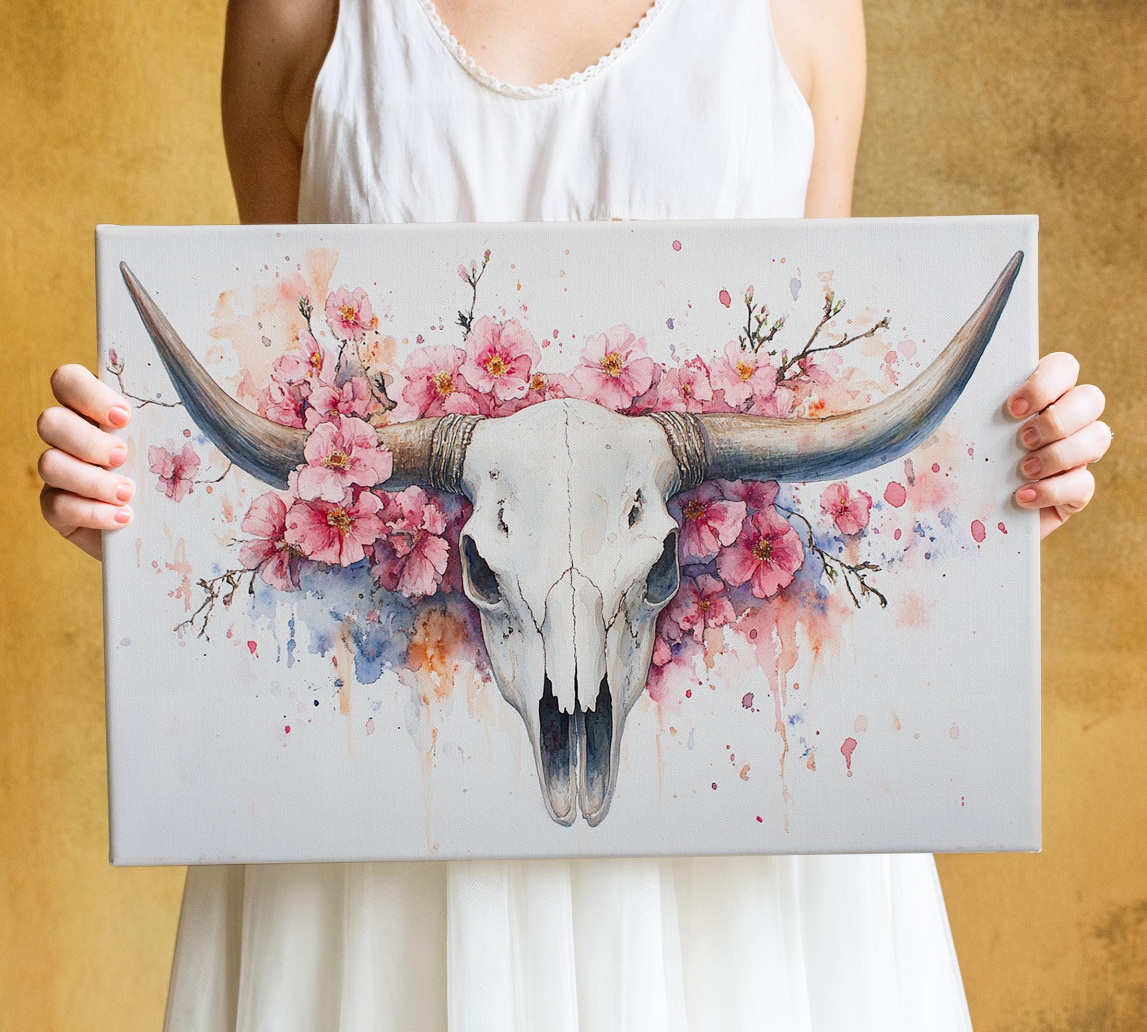 A person is holding a framed artwork featuring a white skull with large horns and a floral design surrounding it.