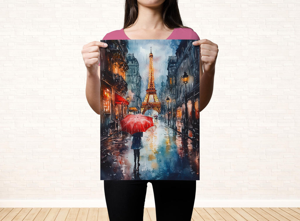 A woman holds up a painting of a rainy street scene with the Eiffel Tower in the background.