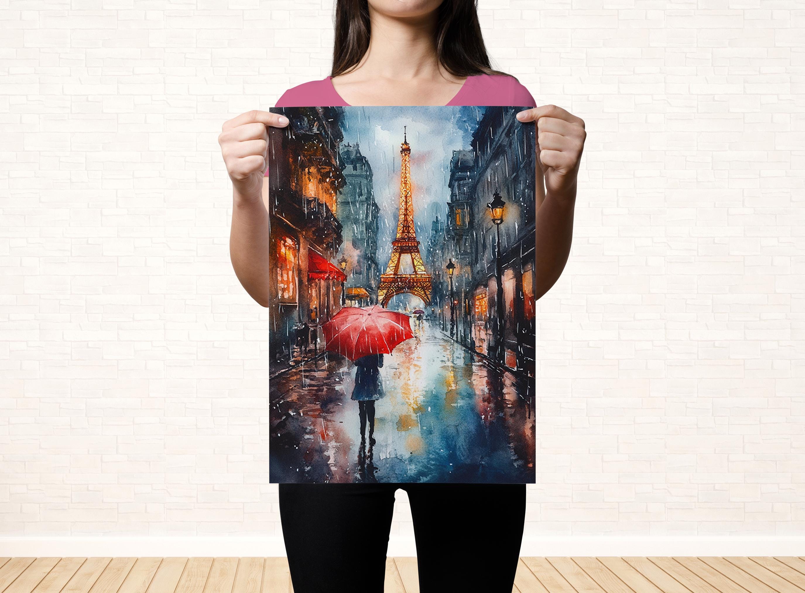 A woman holds up a painting of a rainy street scene with the Eiffel Tower in the background.